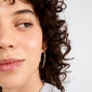 Close-up of a person wearing APRIL medium-size gold-plated hoop earring, showcasing their smooth skin and glossy lips, highlighting the earring's stylish design.
