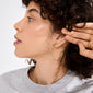 Side profile showcasing APRIL medium-size gold-plated hoop earring, 40 mm diameter, on person with short curly hair, highlighting minimalist, recycled Scandinavian design.
