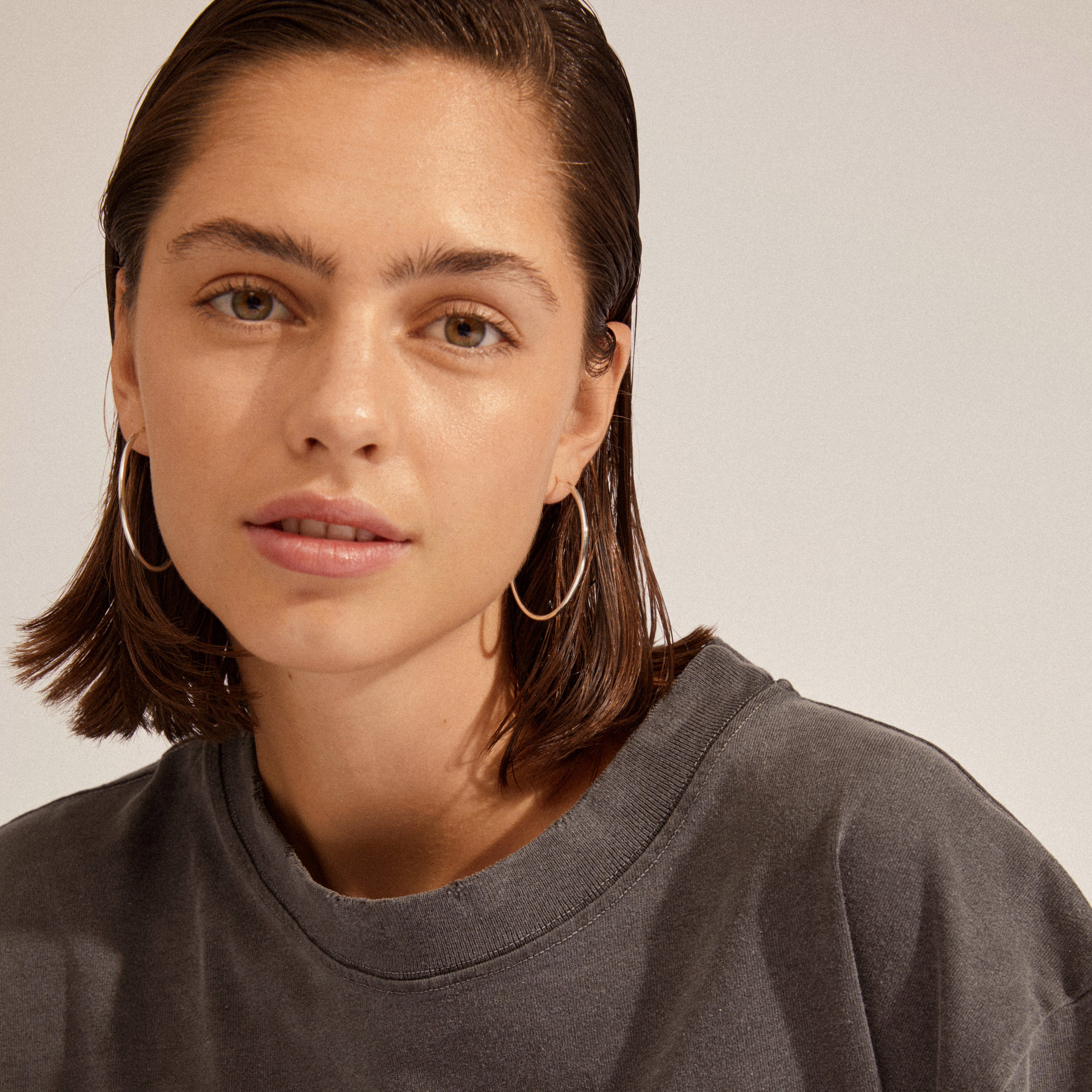 A woman wearing APRIL medium-size hoop earrings, silver-plated, showcasing their elegance and versatility in a close-up portrait.
