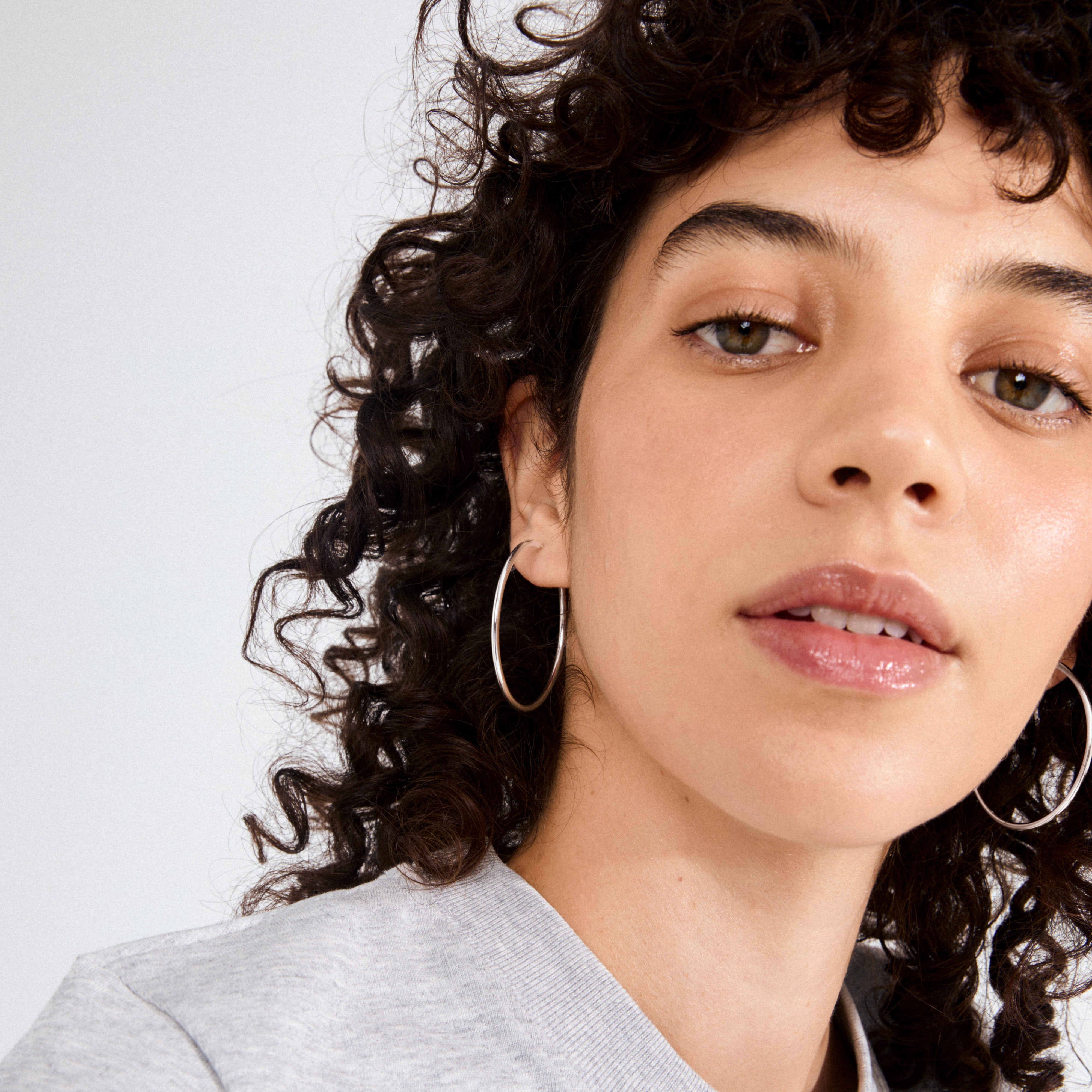 Close-up of person wearing APRIL medium-size hoop earrings, silver-plated, 40 mm diameter, highlighting timeless elegance and simplicity. Perfect for combining with other stylish ear accessories.