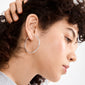 Close-up of a person wearing APRIL medium-size silver-plated hoop earring, highlighting its elegant simplicity against their curly dark hair and naturally glowing skin.