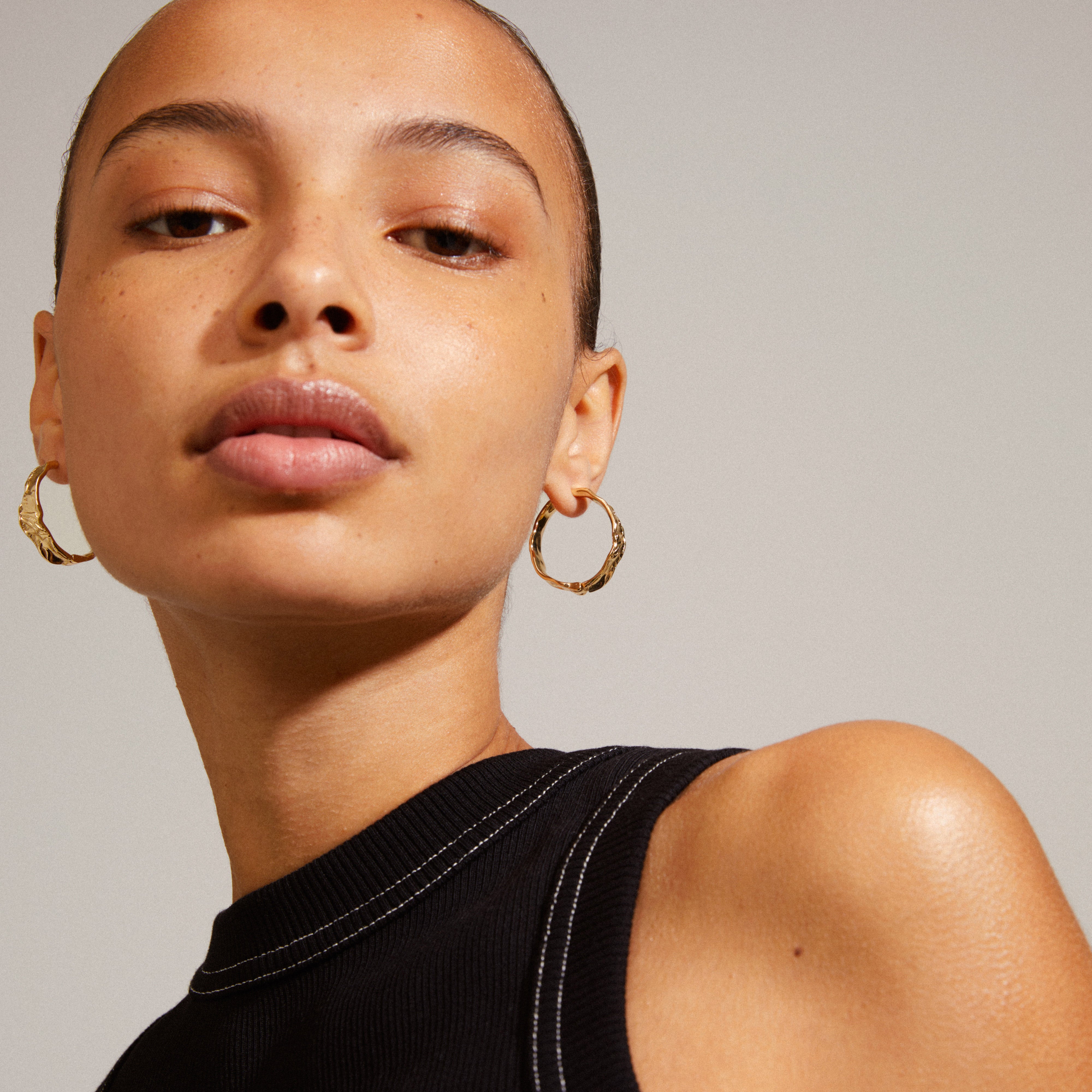 Woman wearing JULITA gold-plated hoop earrings, showcasing their twisted design and wavy lines for a chic, versatile look. Perfect for trendy, personal style seekers.