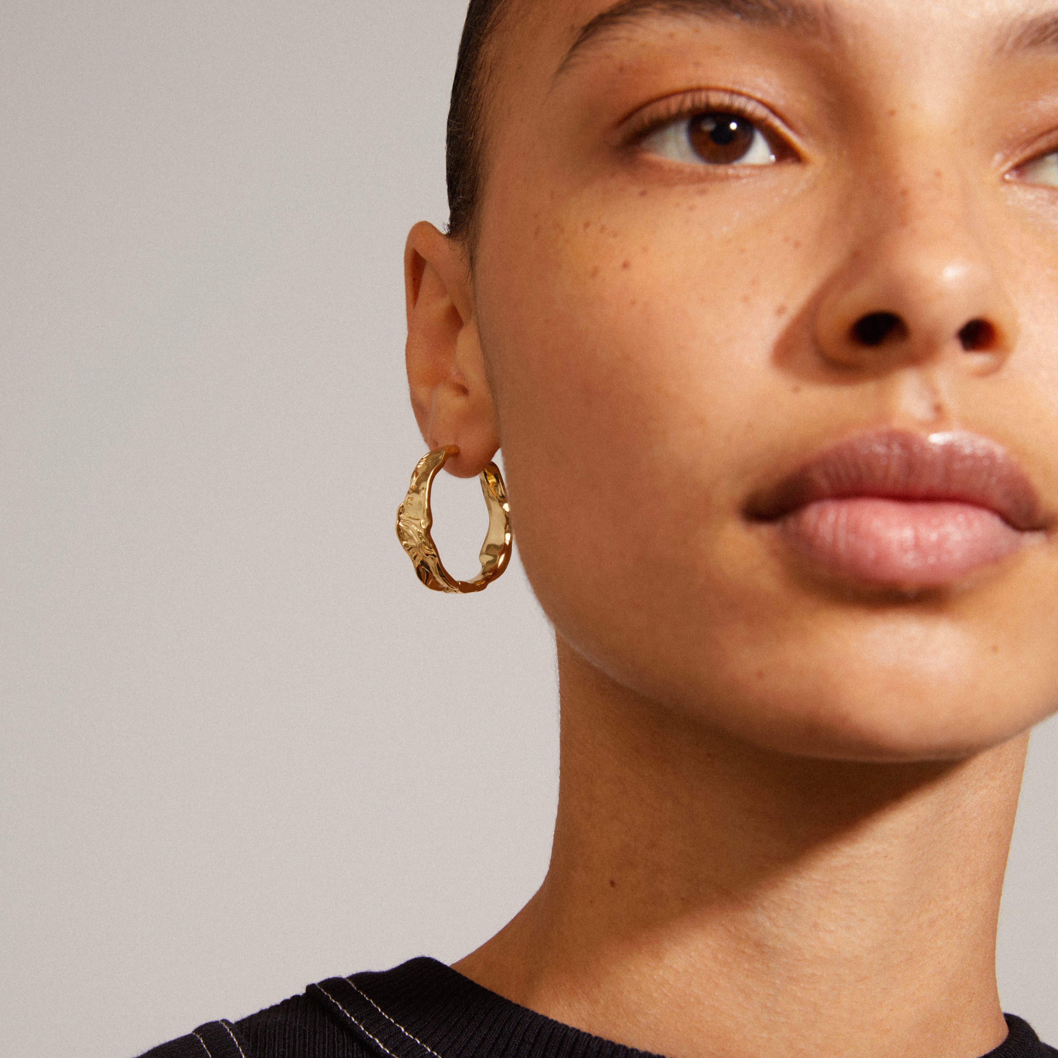 Woman wearing JULITA gold-plated hoop earrings with a twisted design, showcasing a classic and versatile accessory by Pilgrim.