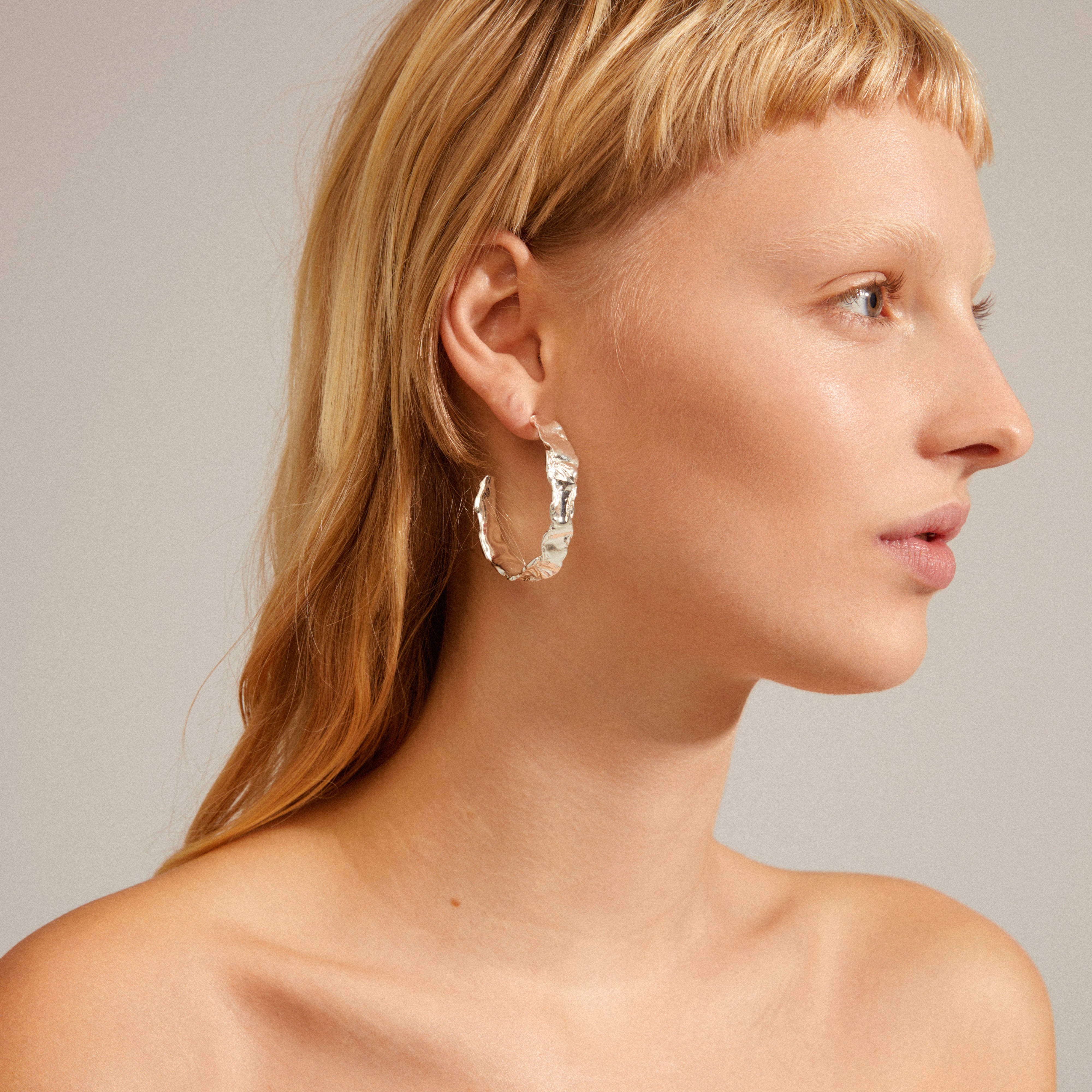 Close-up of a woman's ear wearing Pilgrim's JULITA silver-plated semi-hoop earrings, showcasing their unique, organic design and handcrafted feel.
