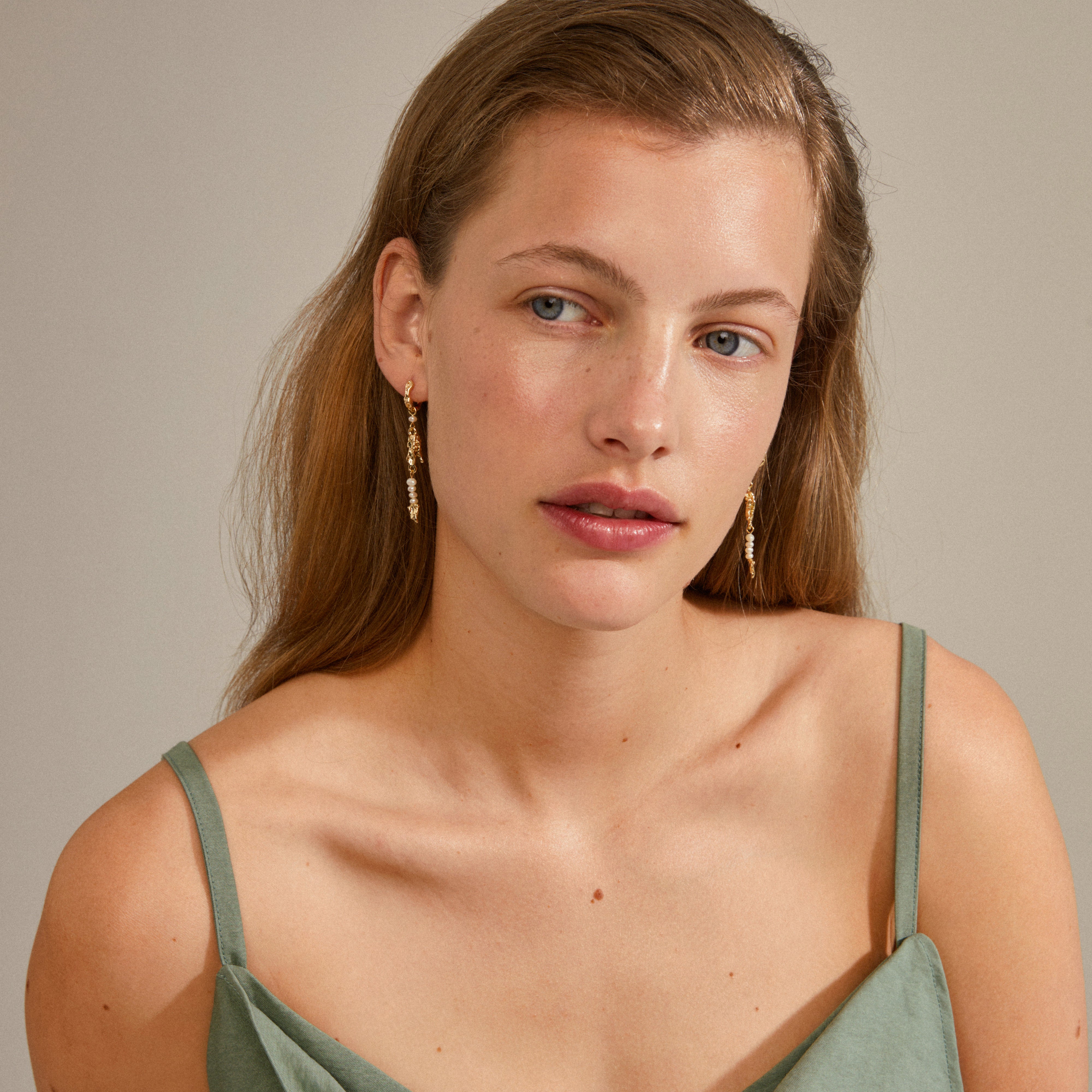 NIYA freshwater pearl earrings gold-plated, featuring organic shapes and genuine pearls, worn by a woman with long hair, adding playful flair.