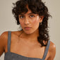 Woman with curly hair wearing a grey dress, showcasing Pilgrim's NIYA earrings in multi-coloured gold-plated design, emphasizing their handcrafted and summery aesthetic.