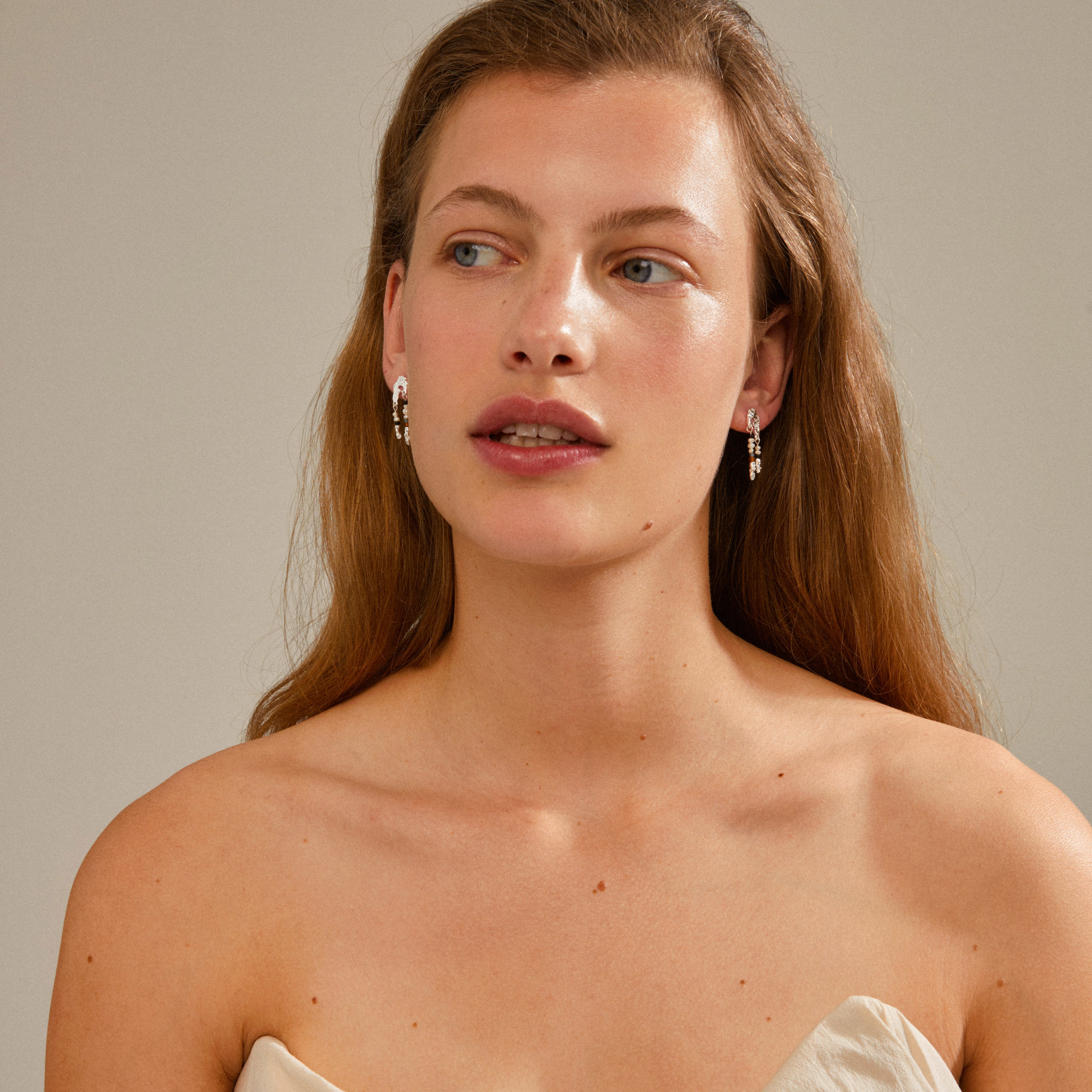 Woman wearing NIYA earrings, multi-coloured/silver-plated, with a handcrafted feel, highlighting her red hair and sun-kissed skin, embodying Pilgrim's Scandinavian style.