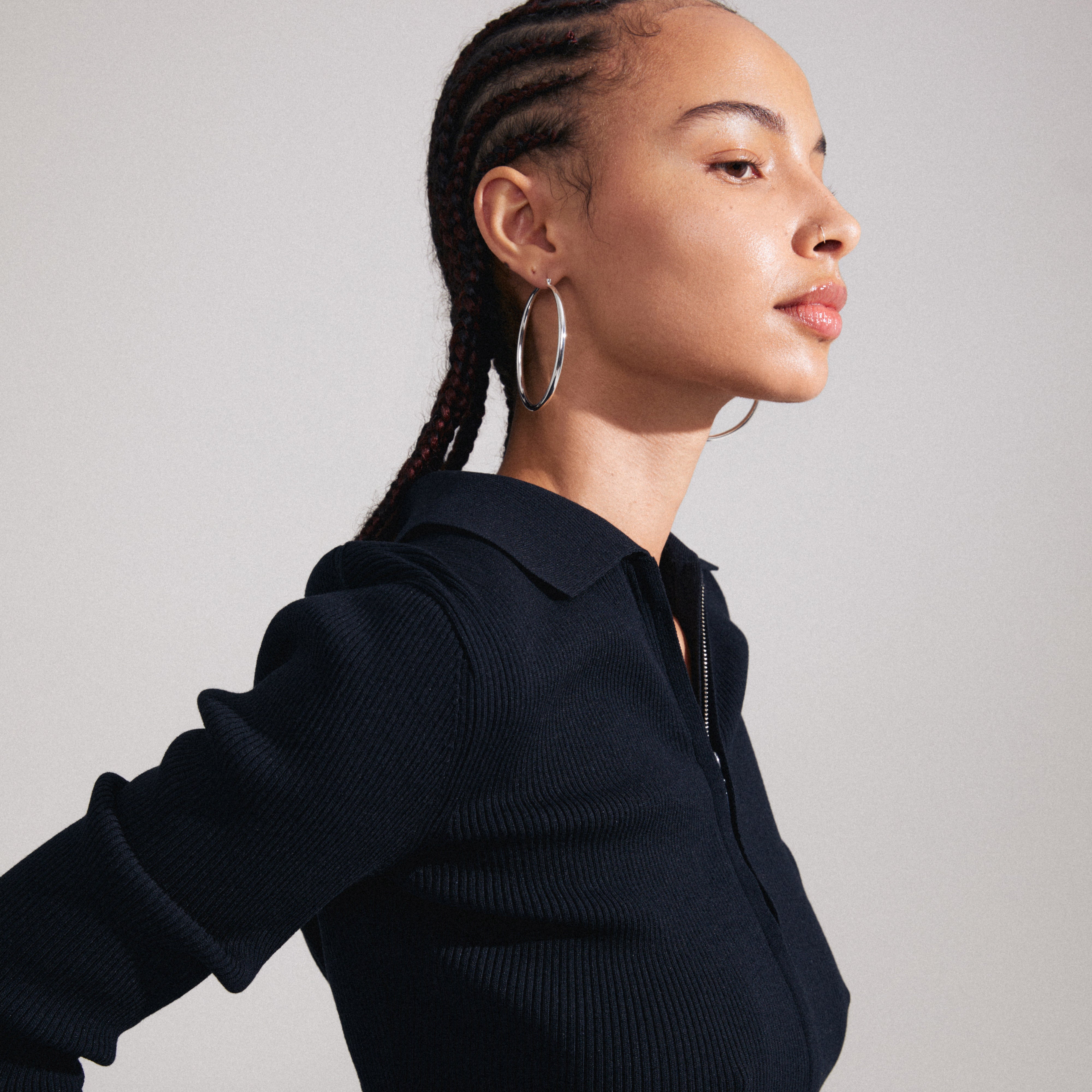 Woman with braided hair wearing PRIYA large silver-plated hoop earrings, showcasing their elegant, timeless design. Perfect for both business and casual looks.
