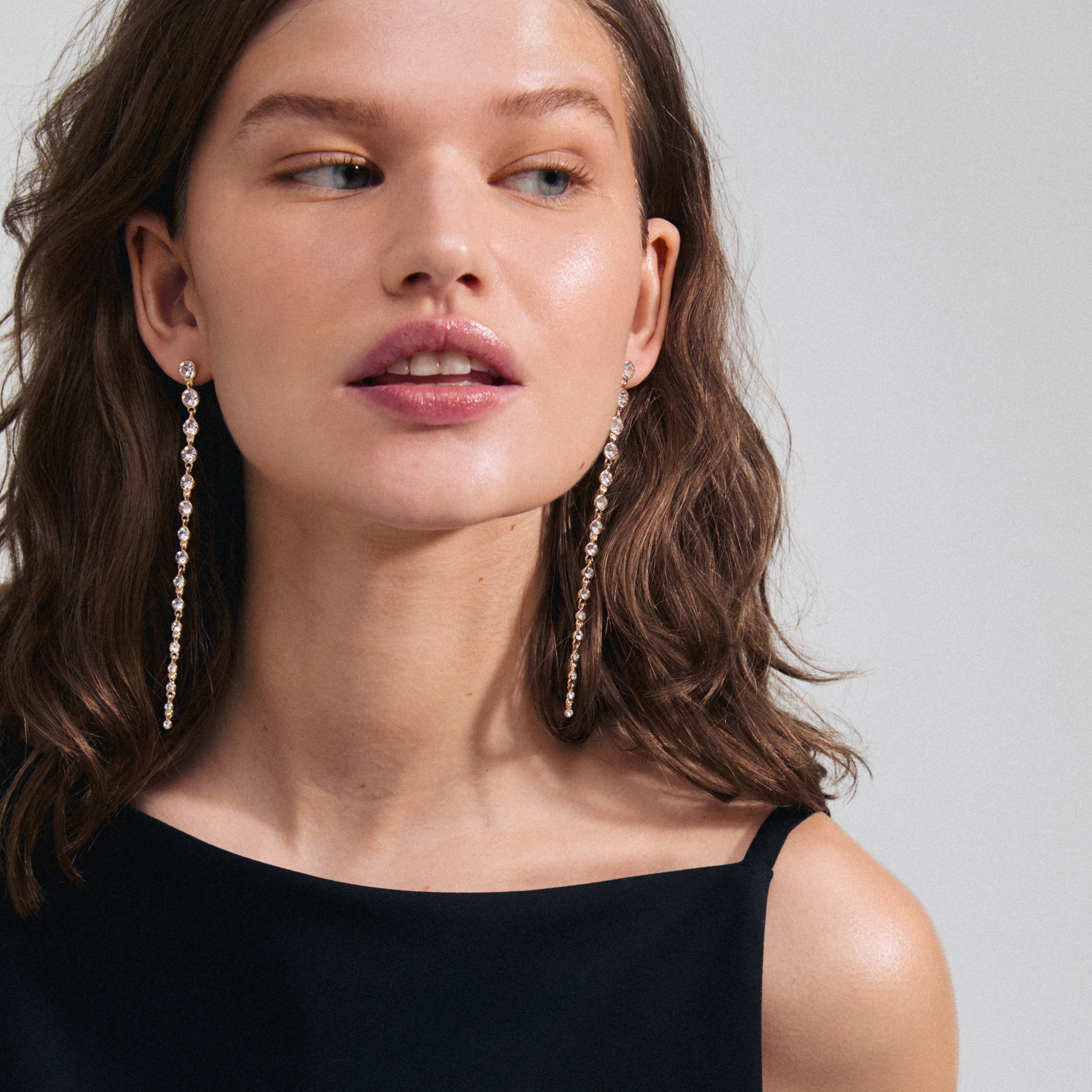 REAGAN crystal earrings gold-plated, featuring long chains of sparkling Preciosa crystals, worn by a woman in a black dress, showcasing elegant, sustainable design.