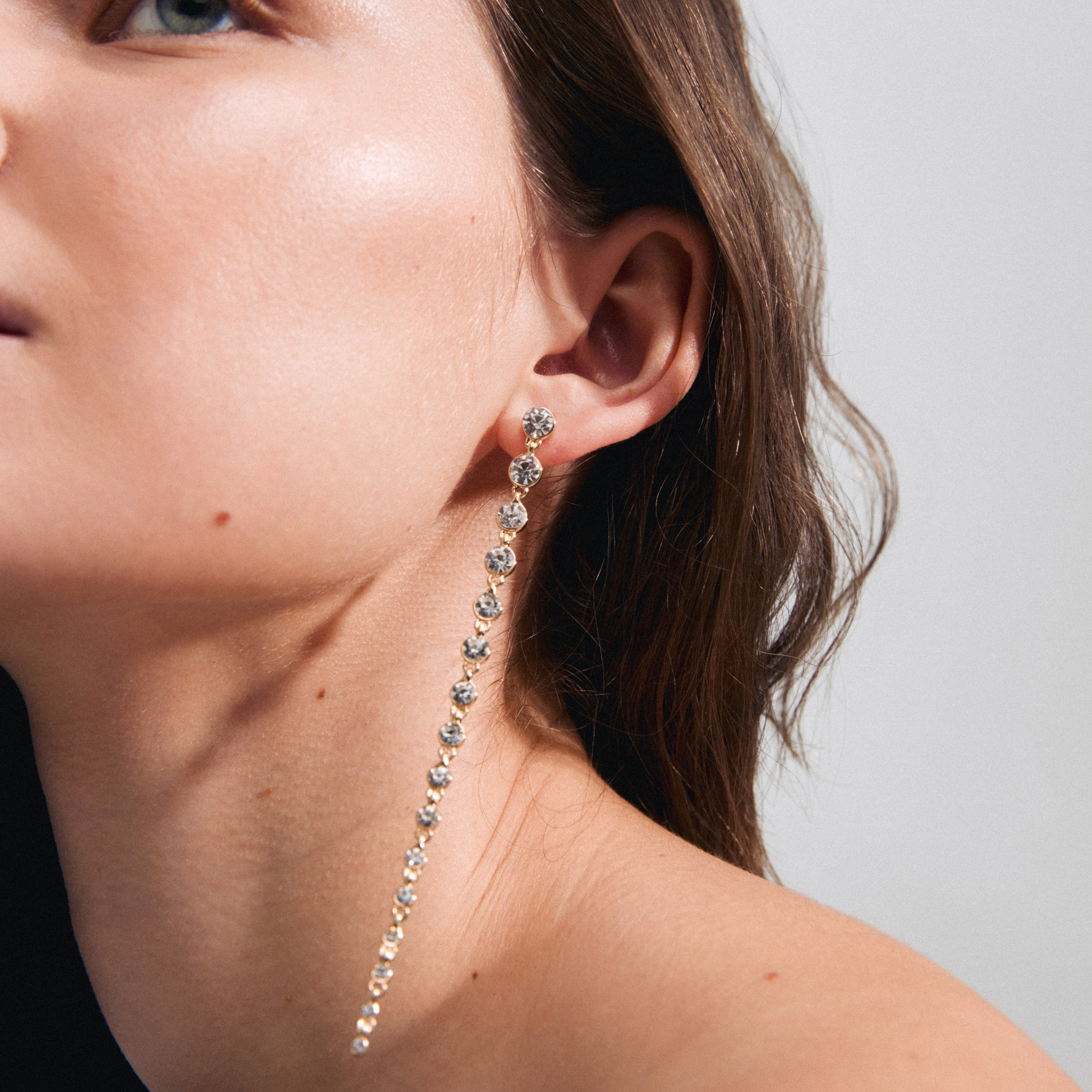 REAGAN crystal earrings gold-plated featuring long chains of sparkling Preciosa crystals, worn by a woman, showcasing their elegant and impactful design.