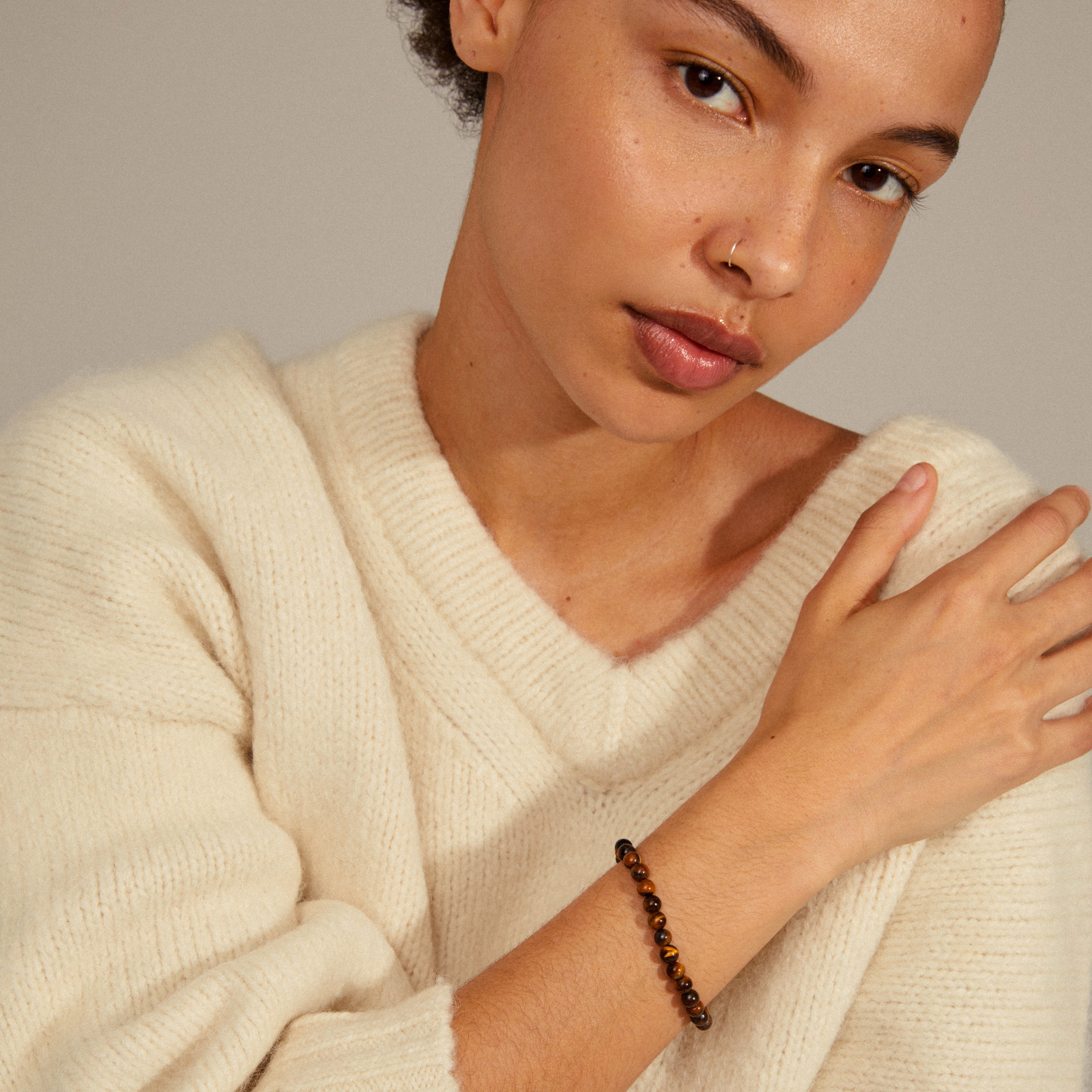 Woman showcasing the POWERSTONE bracelet, featuring round Tiger Eye stones on elastic, designed to counteract stress and imbalance, embodying Scandinavian quality and style.