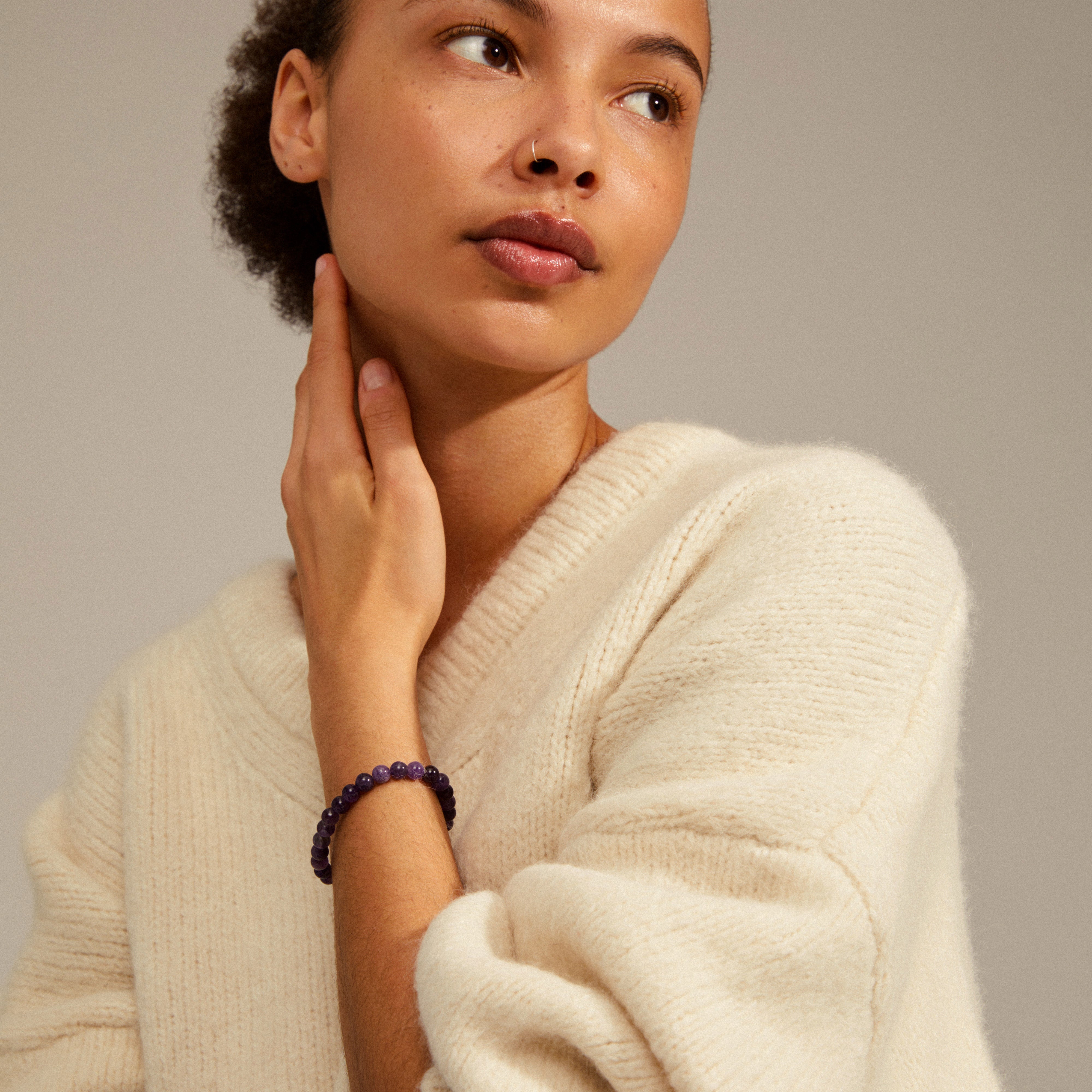 Woman wearing a white sweater showcases the POWERSTONE bracelet with amethyst stones, highlighting its meditative and calming properties.