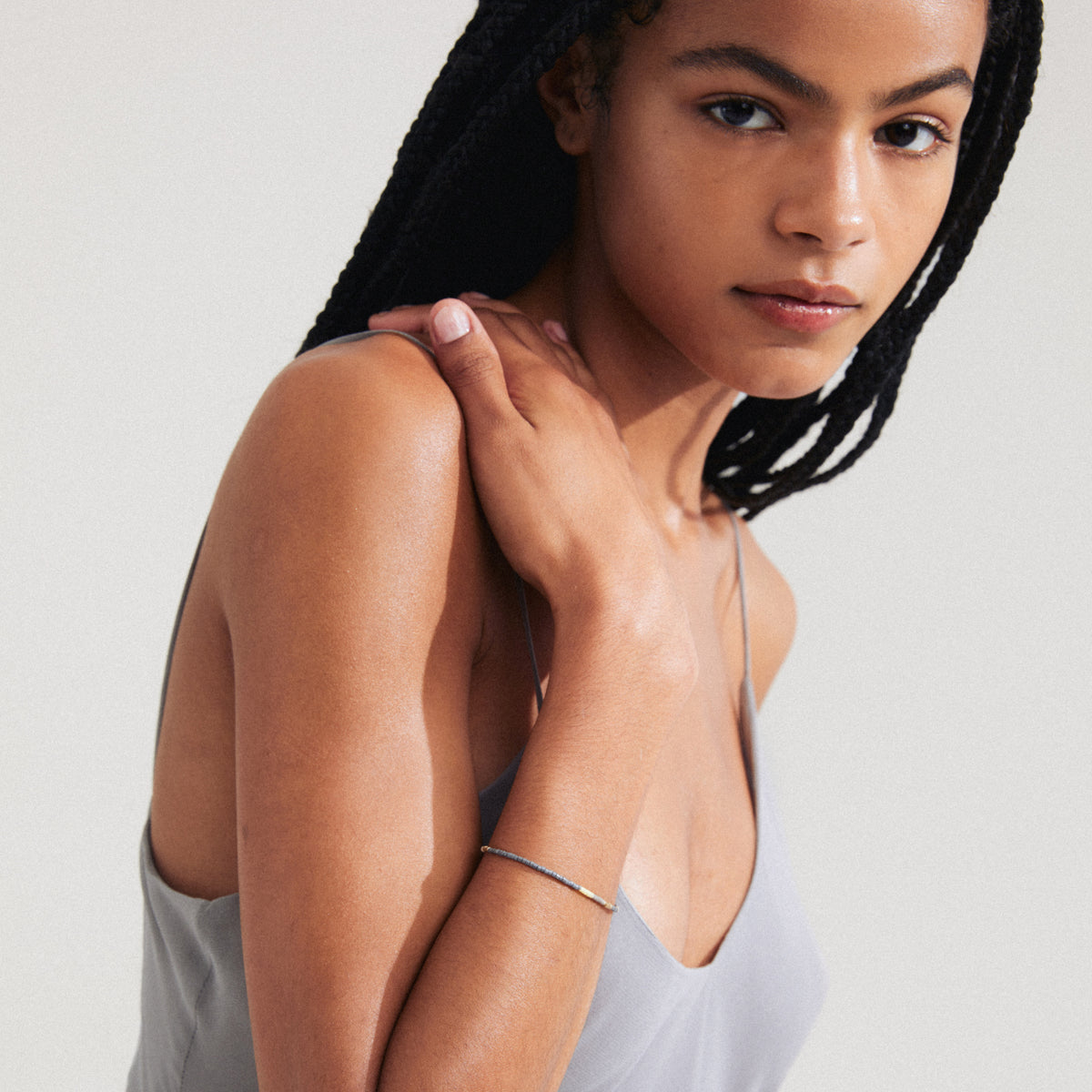Woman with braided hair wearing the ALISON bracelet in silver-plated, featuring grey glass beads, perfect for creating a boho-chic, stackable accessory look.