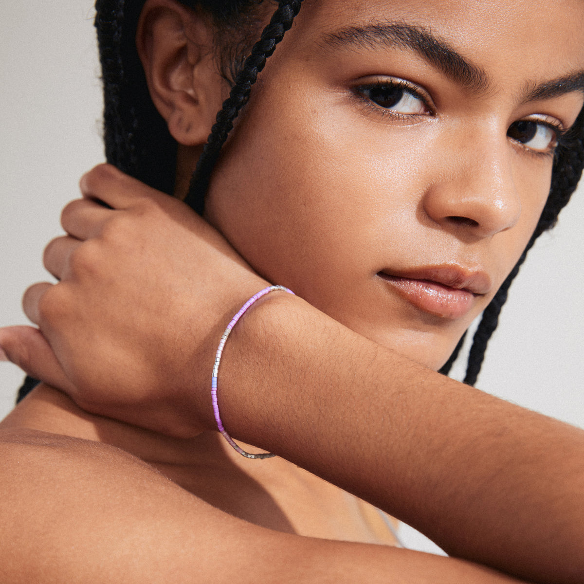 Woman with braids showcasing the ALISON bracelet in purple and silver-plated, featuring purple and grey glass beads on a durable lycra elastic band.