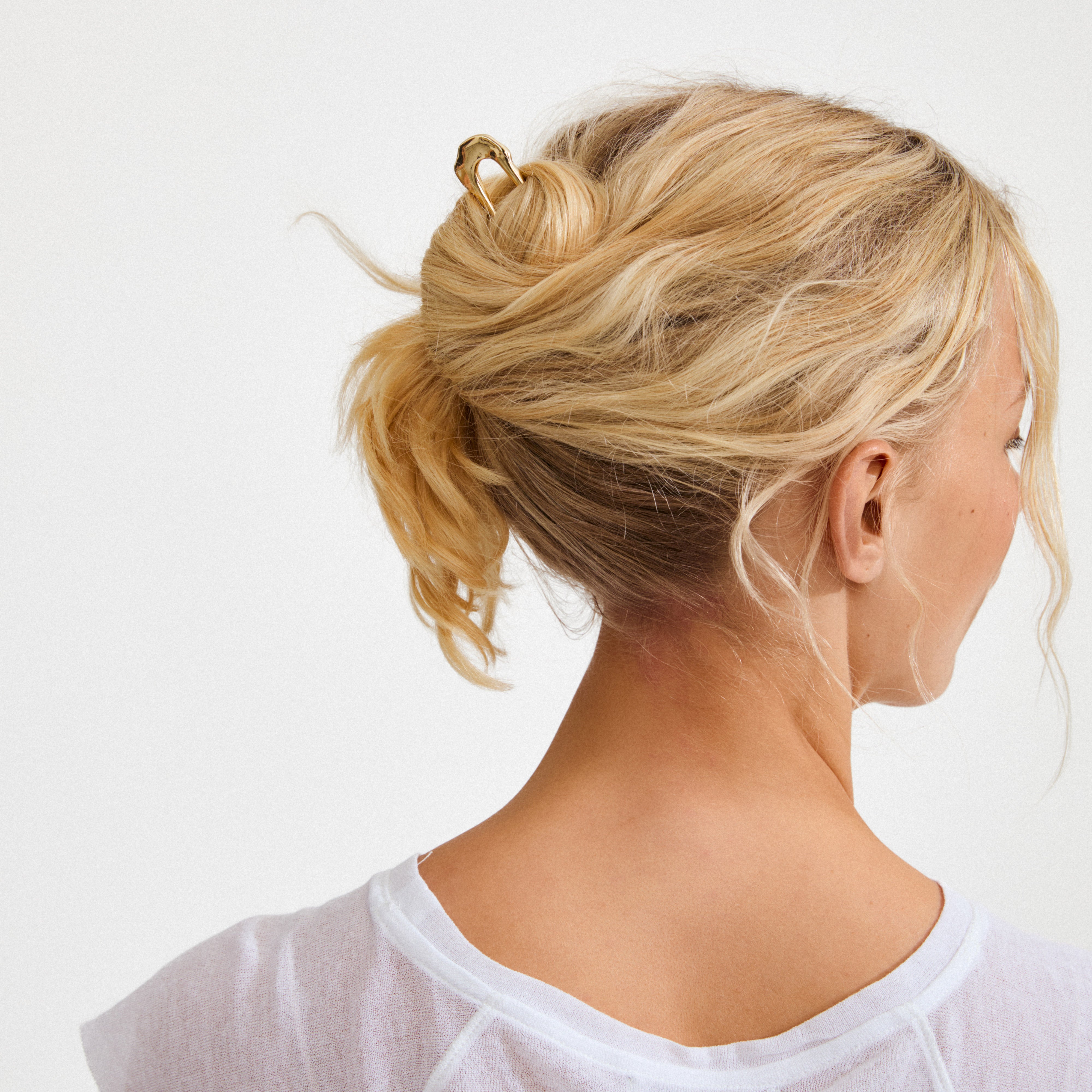 Gold-plated AMARIS hairpin securing a loose bun on a person with blonde hair, showcasing minimalist elegance and understated luxury.