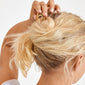 Blonde hair in a twisted bun is secured with the 10 cm gold-plated AMARIS hairpin from Pilgrim, showcasing chic minimalist design and effortless elegance.