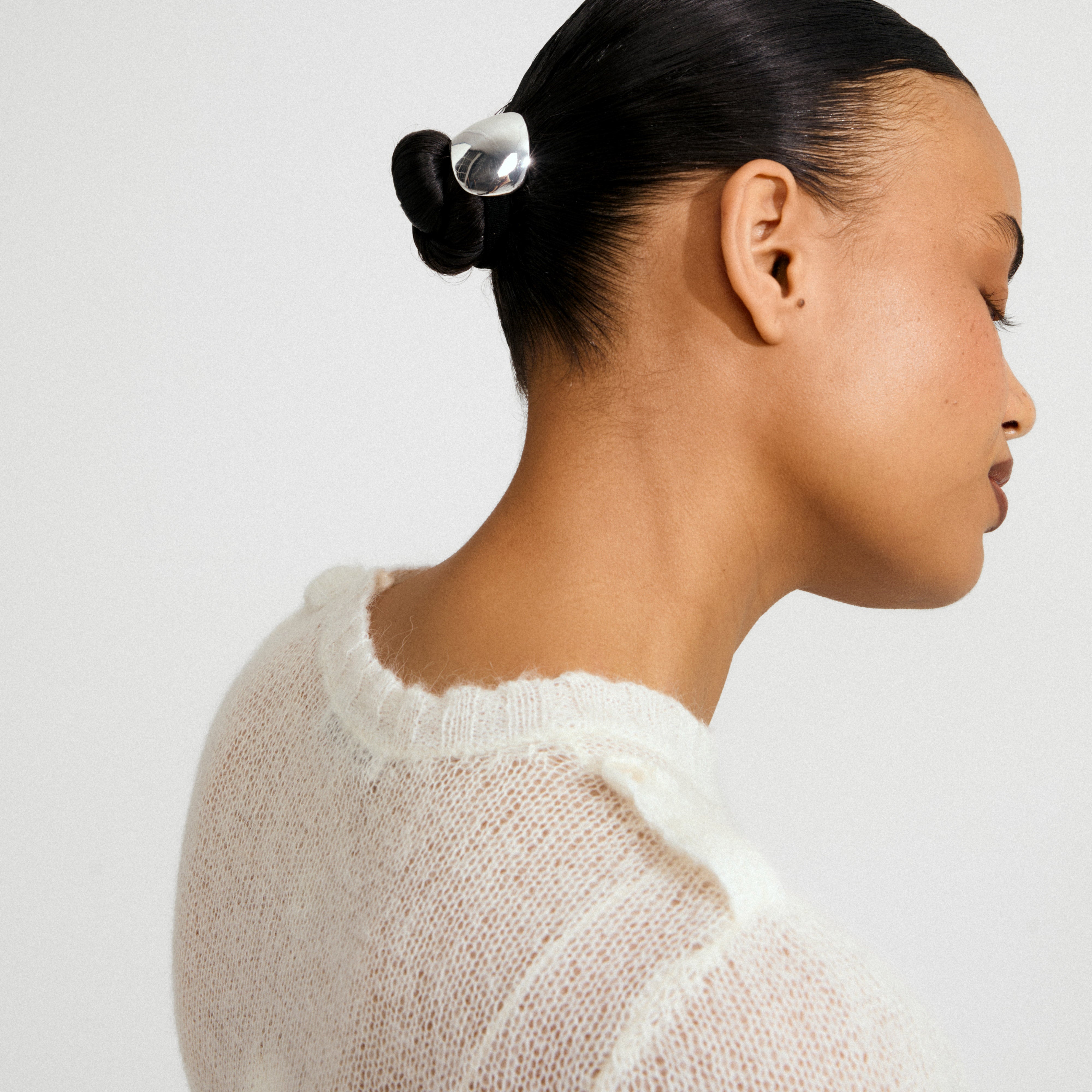 Woman wearing AMARIS hair accessory, a silver-plated elastic, styled in a sleek bun, paired with a sheer white sweater. Effortlessly blends function and fashion.