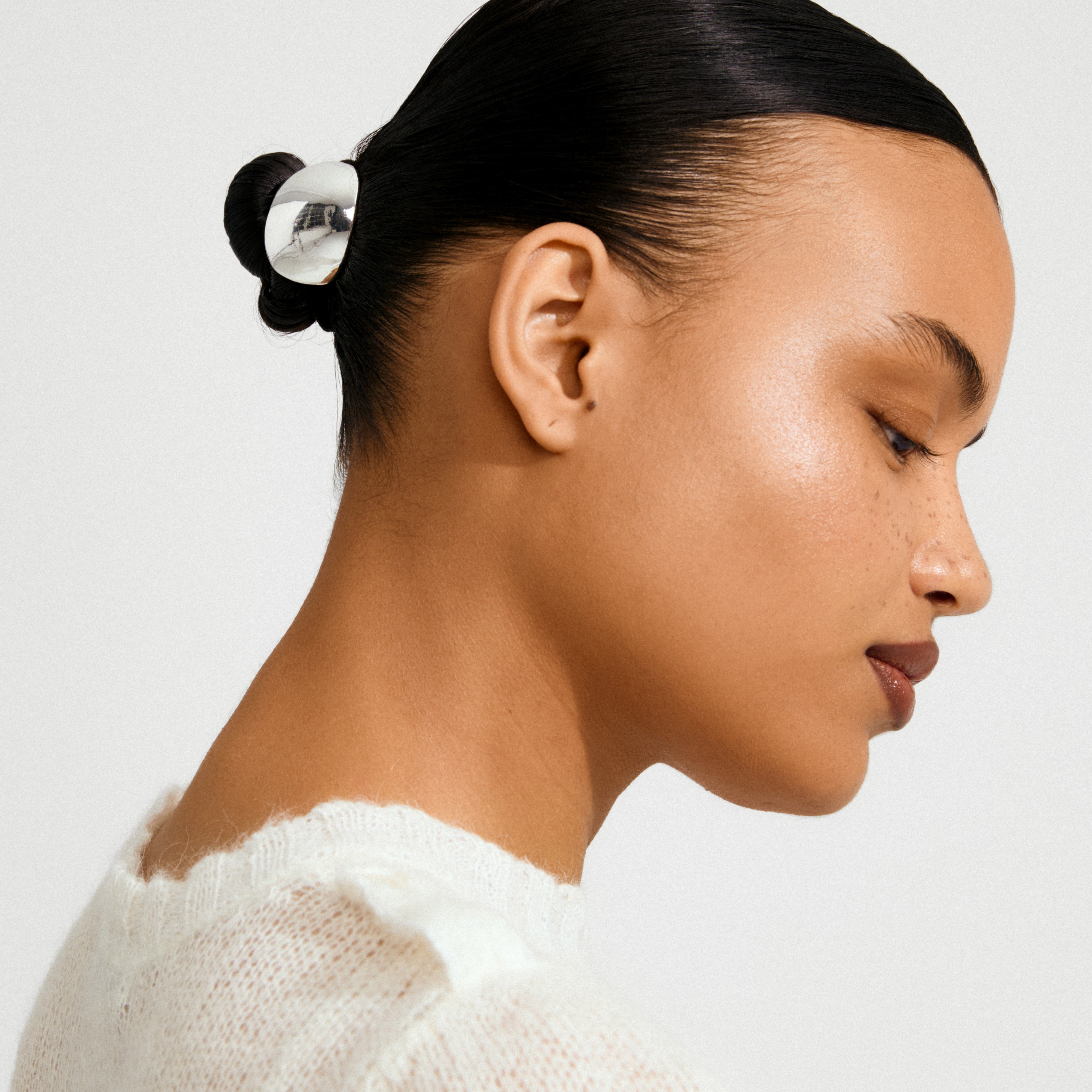 Young woman with sleek, slicked-back bun featuring the AMARIS hair accessory, a shiny silver-plated clip from Pilgrim, adding a stylish touch to her look.