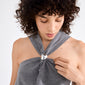 Young woman adjusts grey halter top clasped with a silver heart, highlighting Pilgrim's AMARIS hair accessory, a sleek, silver-plated deco element for stylish hairstyles.