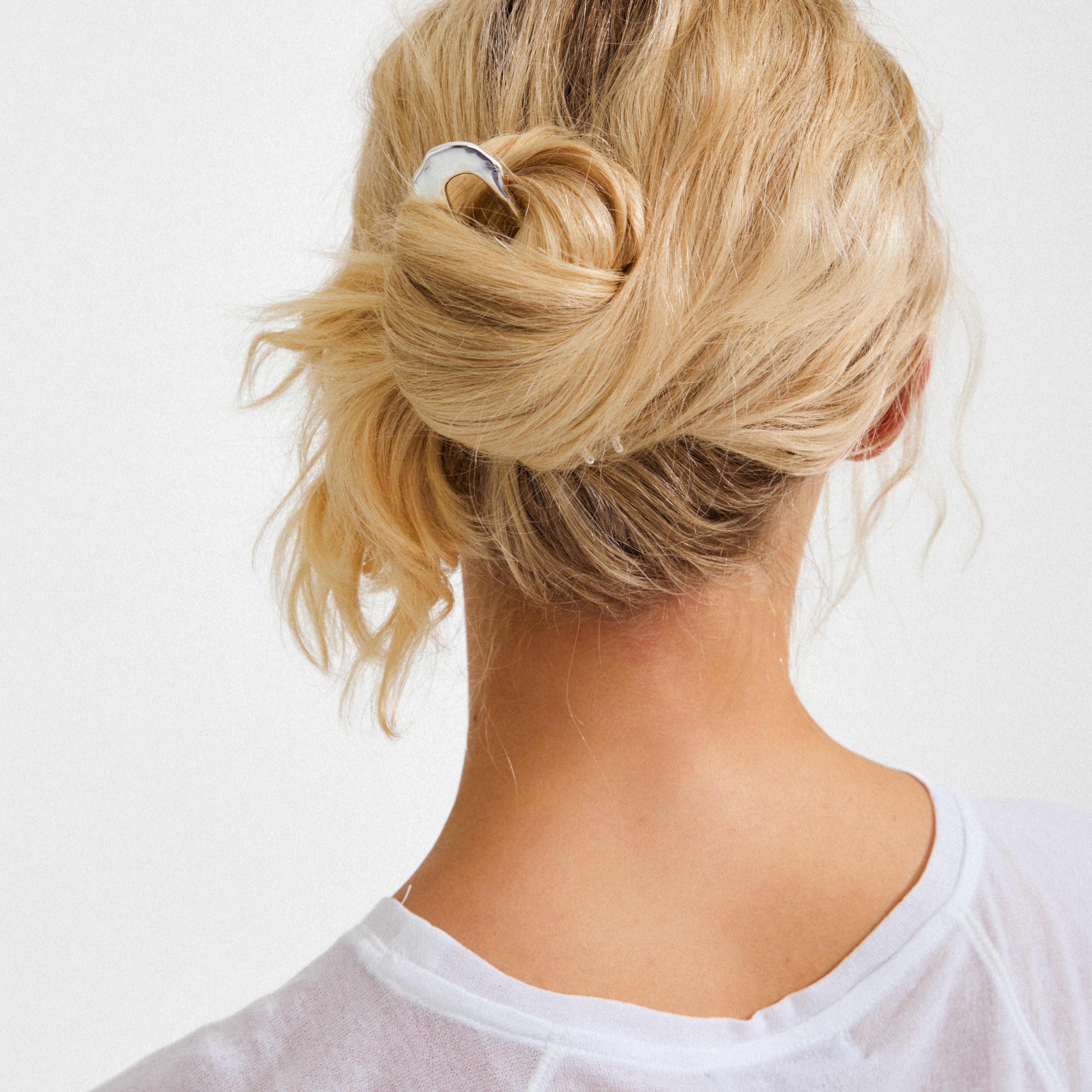 Person with blonde hair in a low bun, secured by the silver-plated AMARIS hair accessory from Pilgrim, showcasing sleek, minimalist design and understated elegance.