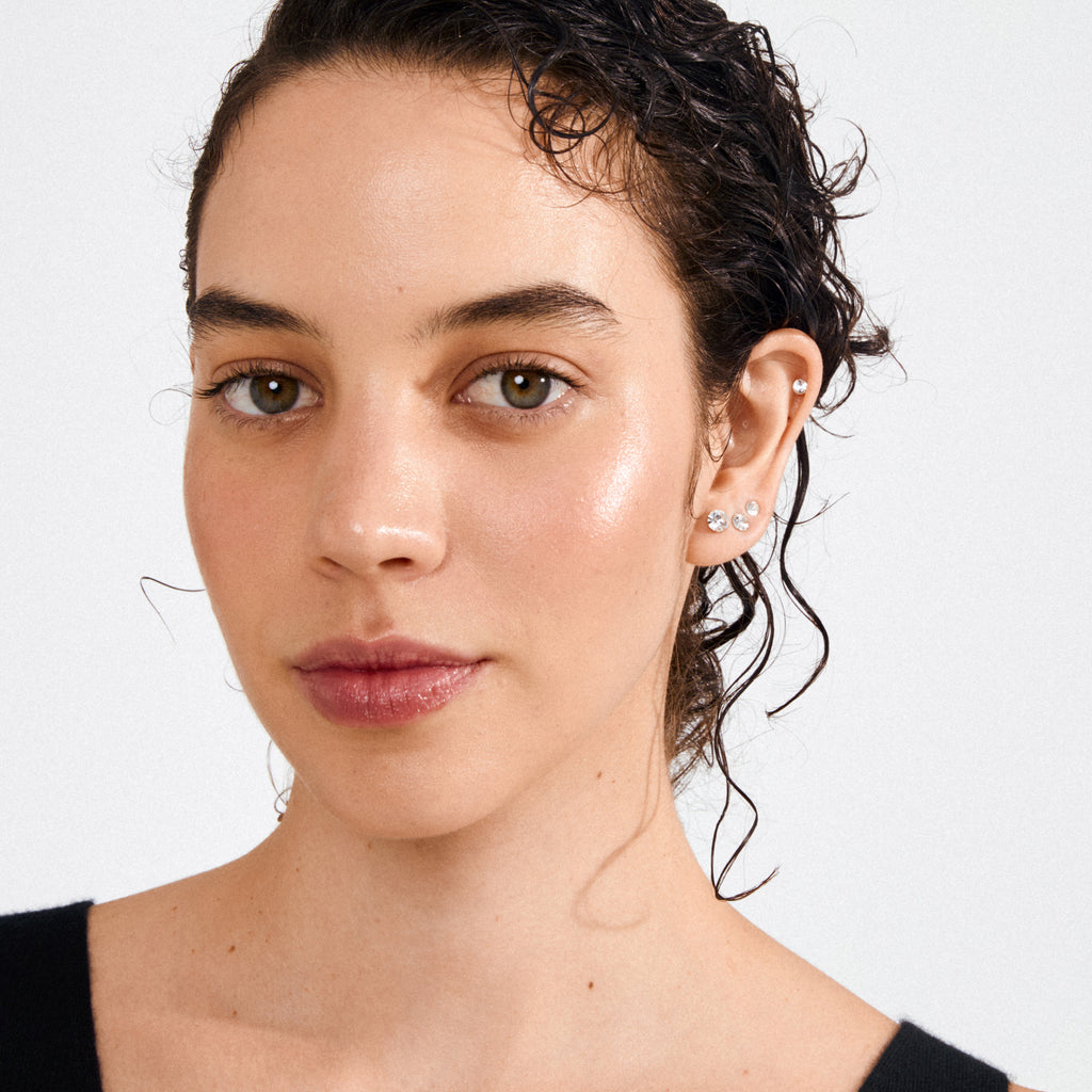 Young woman wearing MILLIE crystal earrings, 3-in-1 set, gold-plated, showcasing three stud sizes on her earlobe and helix, highlighting minimalist and stylish jewelry.