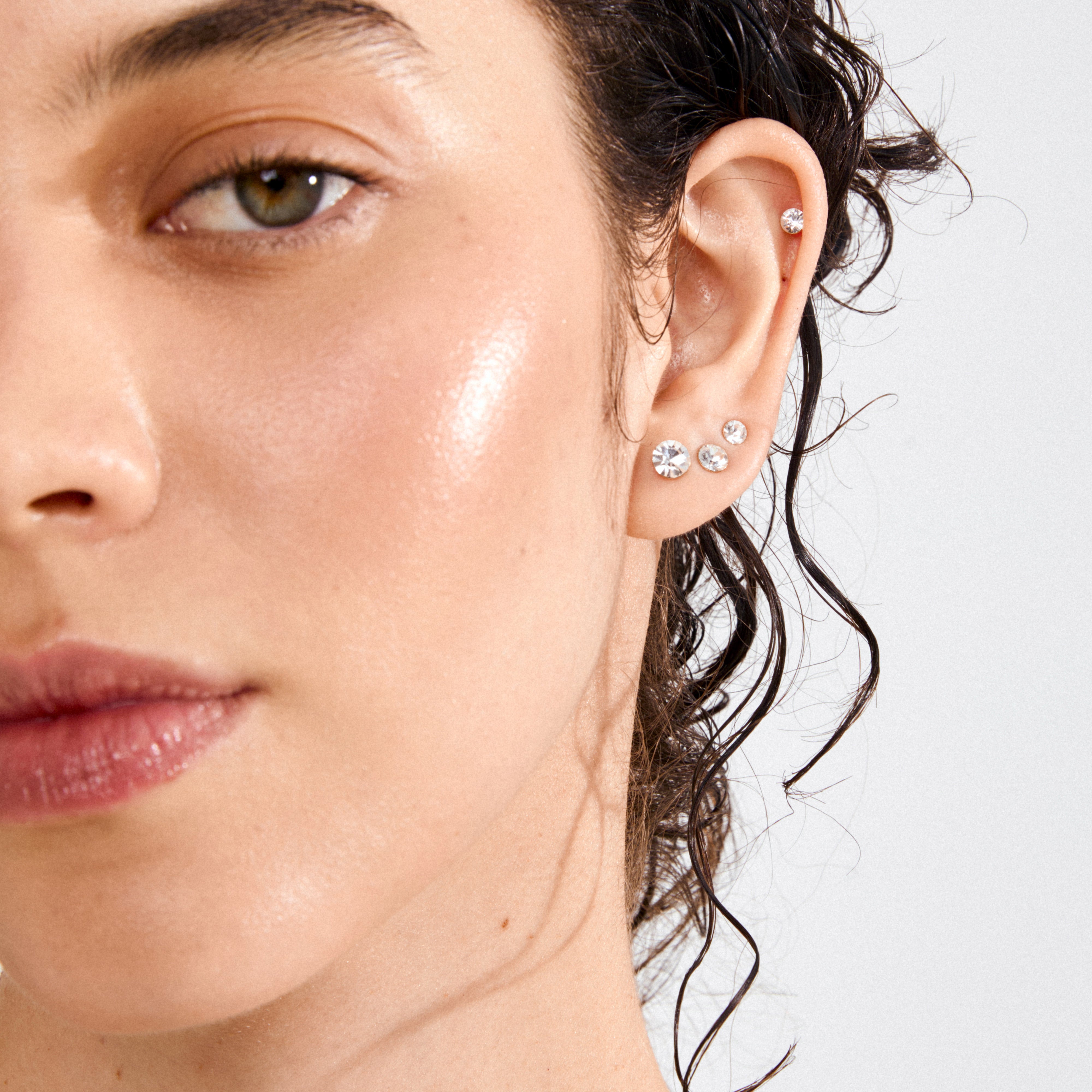 Close-up of a dewy-skinned ear adorned with MILLIE 3-in-1 gold-plated crystal earrings, showcasing various sizes for versatile styling.