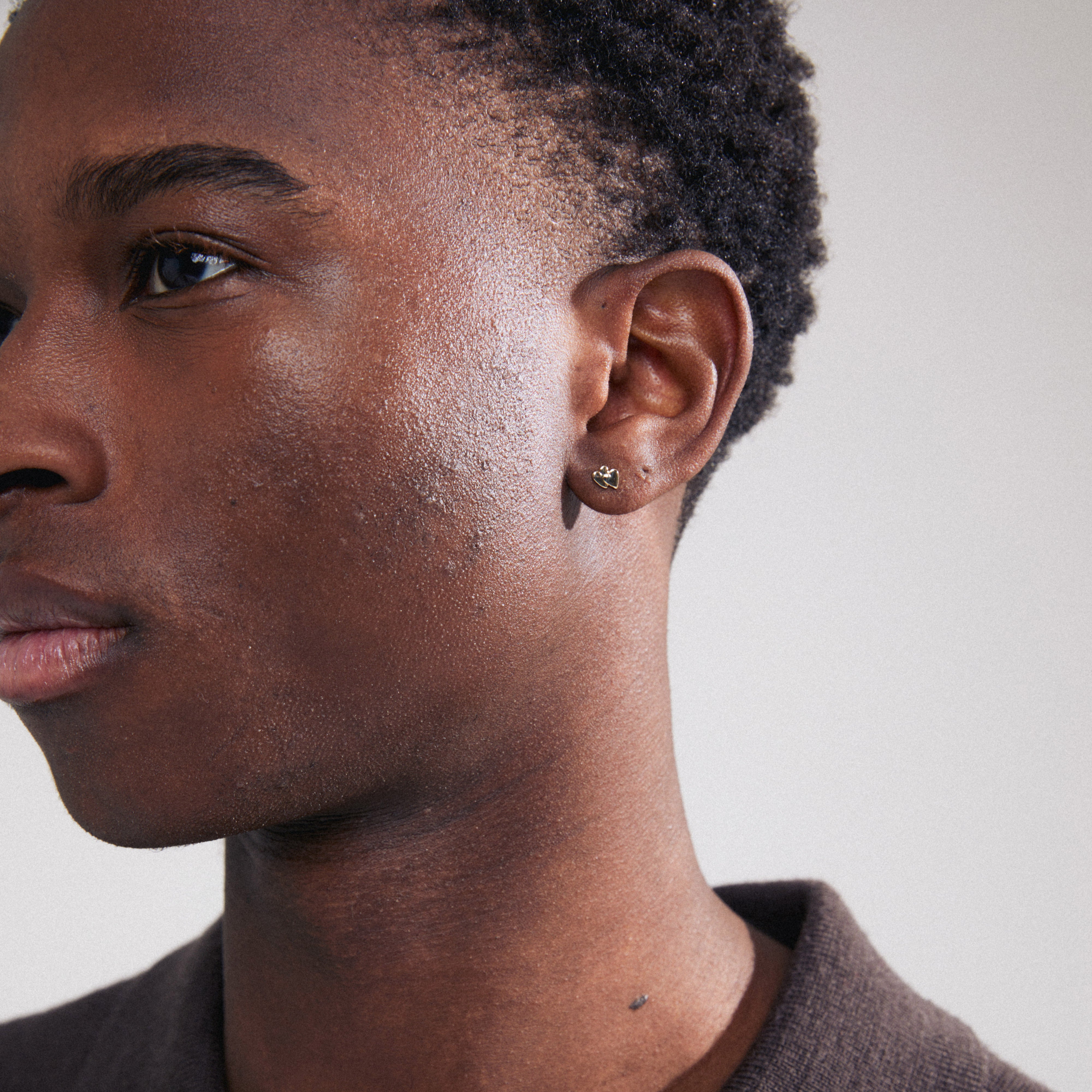 PRISKA single earring gold-plated: Close-up of a man's ear wearing a tiny heart-shaped stud, showcasing a minimalist, trendy design for personalized style.