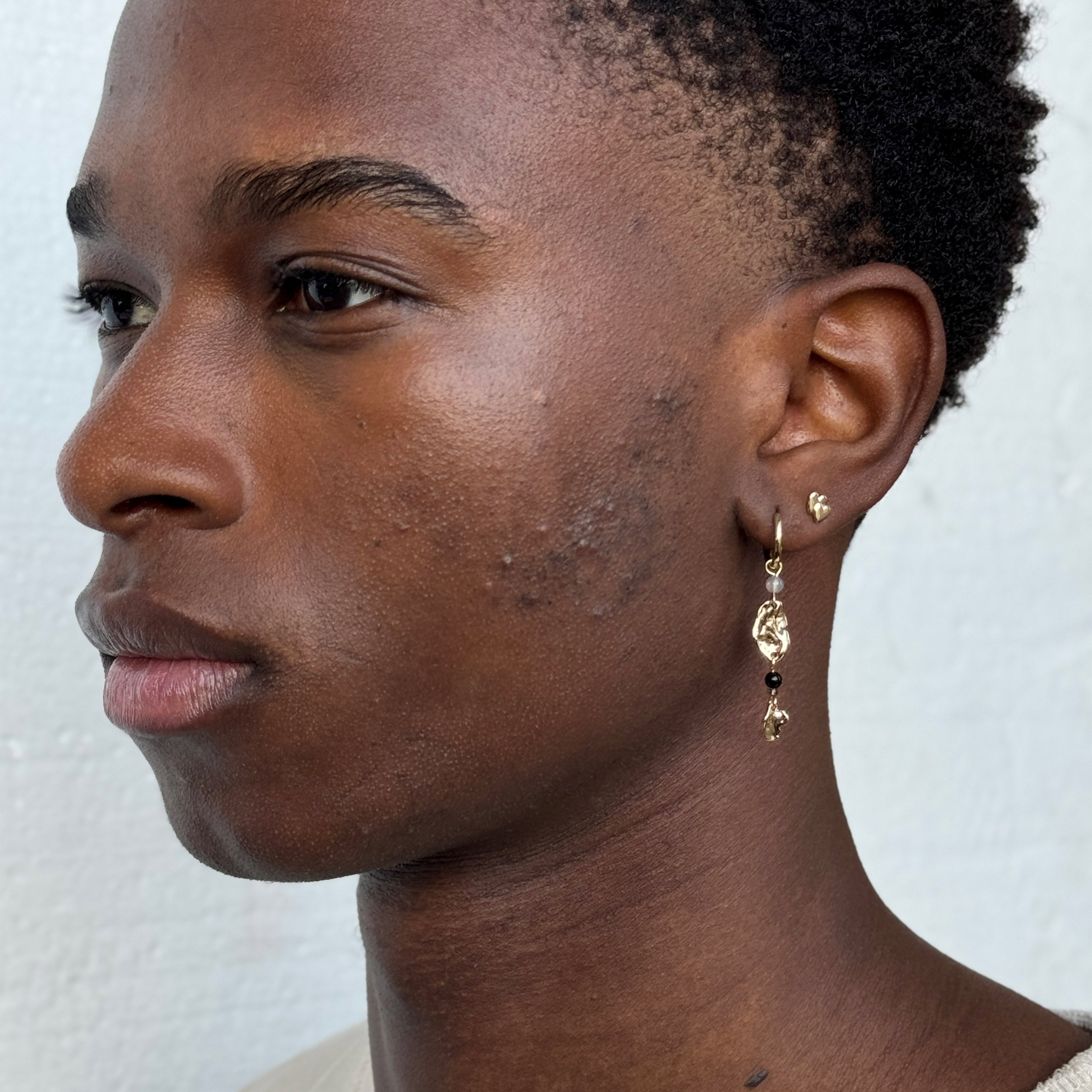 PRISKA single earring gold-plated, features two heart shapes, worn by a man with earrings, showcasing Pilgrim's blend of timeless and trendy Danish design.