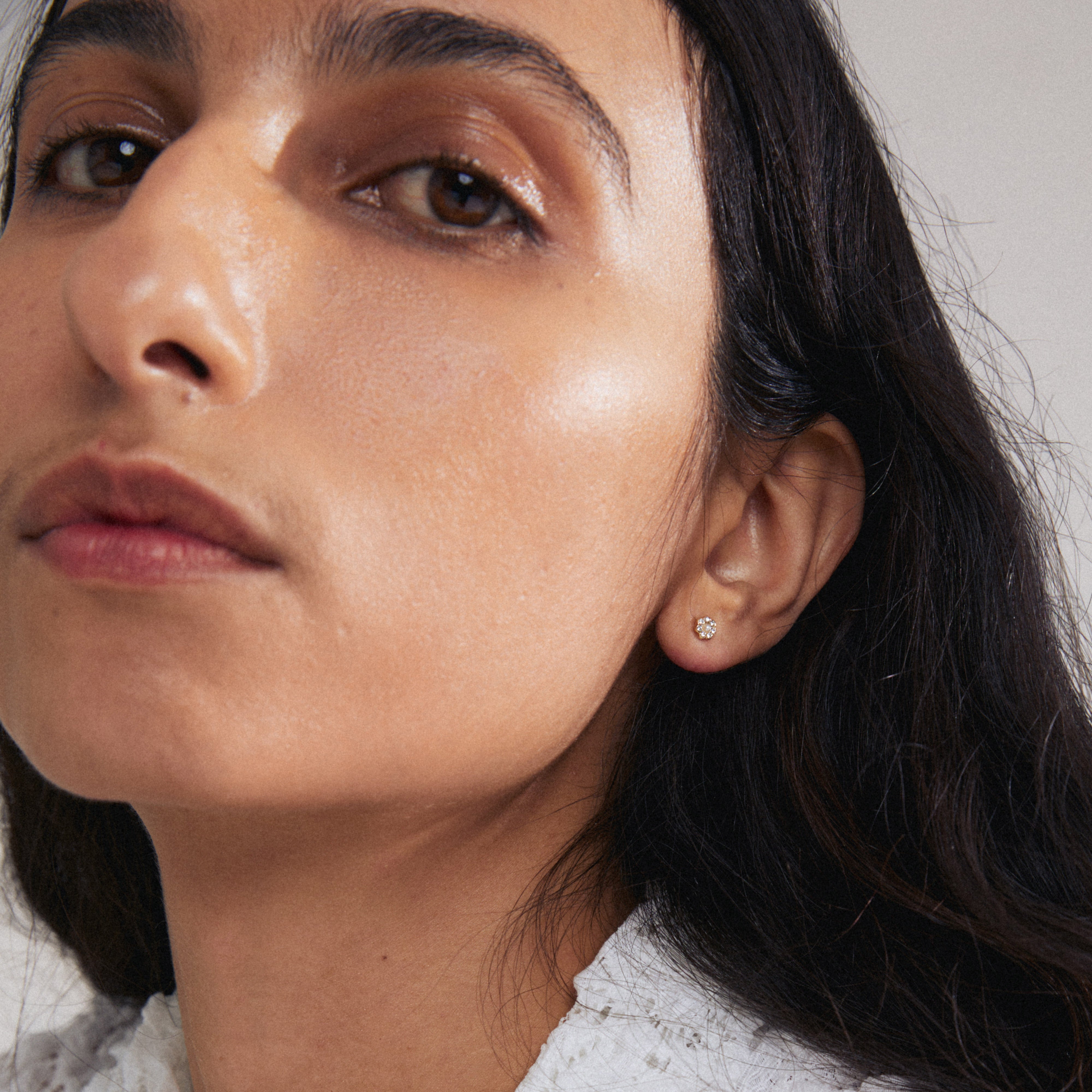 NIKOLETA single earring gold-plated, showcasing a floral design with a pearlescent bead and sparkling crystals, worn by a woman with long hair.