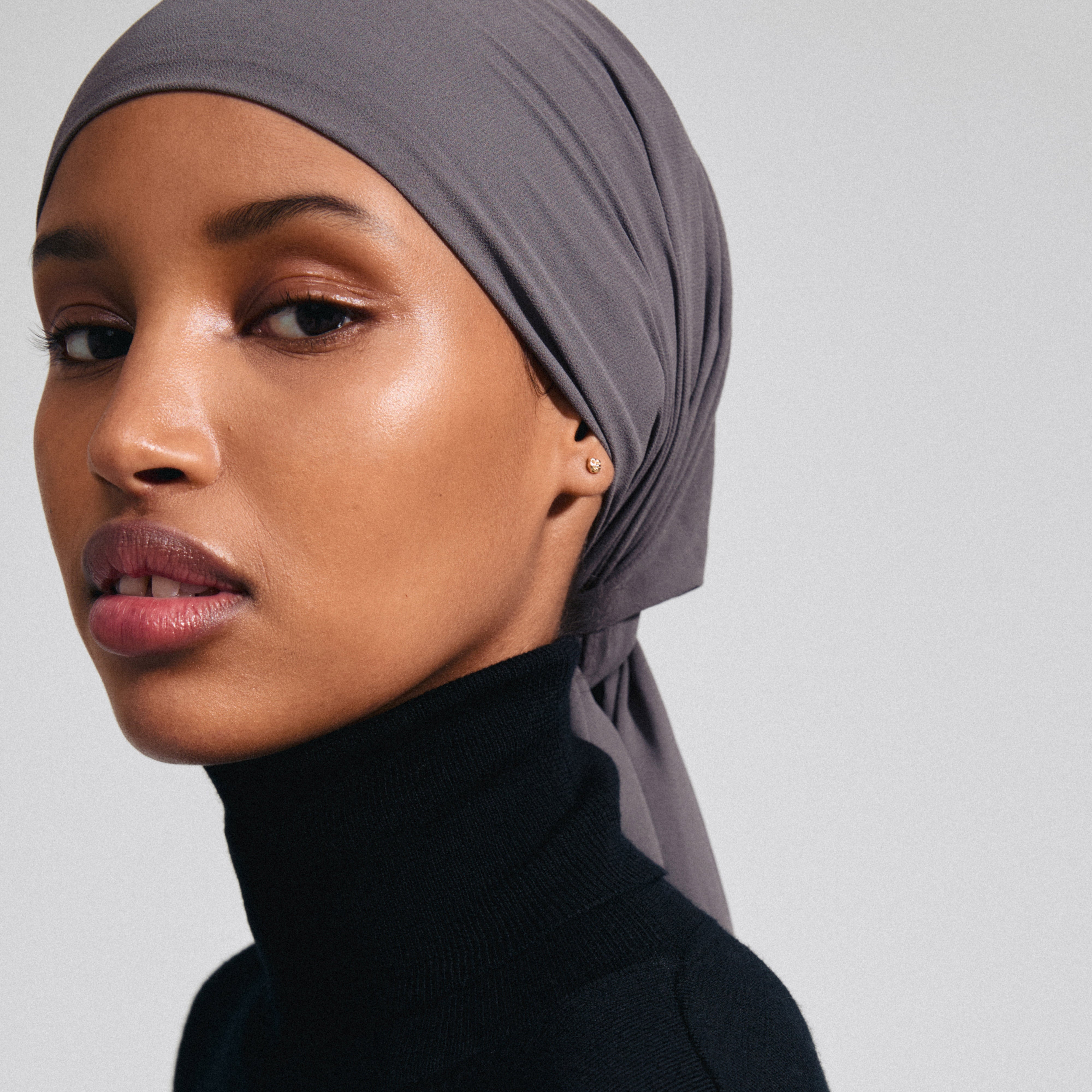 Woman wearing a headscarf and a black turtleneck, showcasing the PELAGIA single gold-plated earring by Pilgrim, highlighting its unique organic shape and rustic surface.