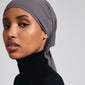 Woman wearing a headscarf and a black turtleneck, showcasing the PELAGIA single gold-plated earring by Pilgrim, highlighting its unique organic shape and rustic surface.