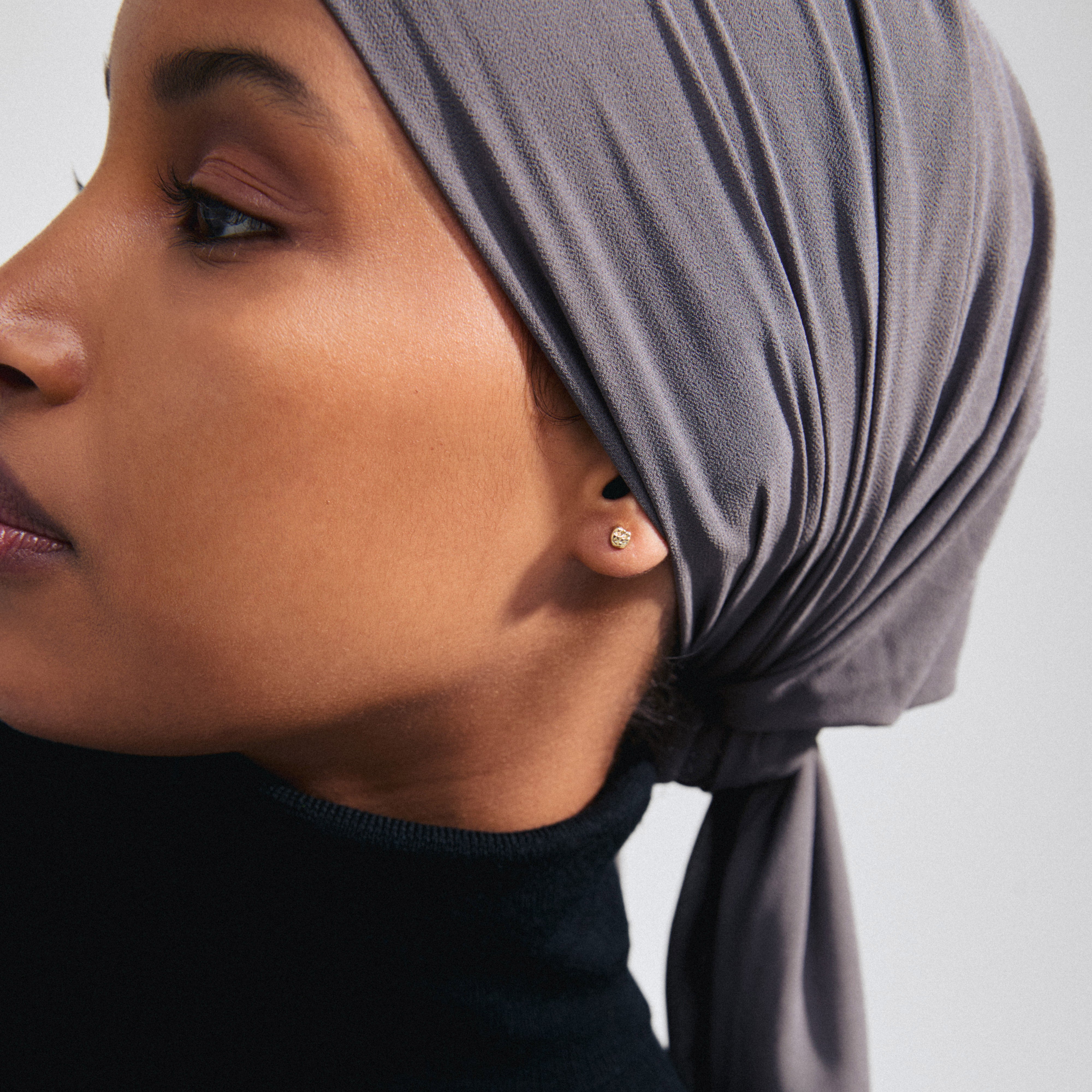 Woman wearing a headscarf showcases the PELAGIA single gold-plated earring from Pilgrim, highlighting its unique, rustic design and sustainable craftsmanship.