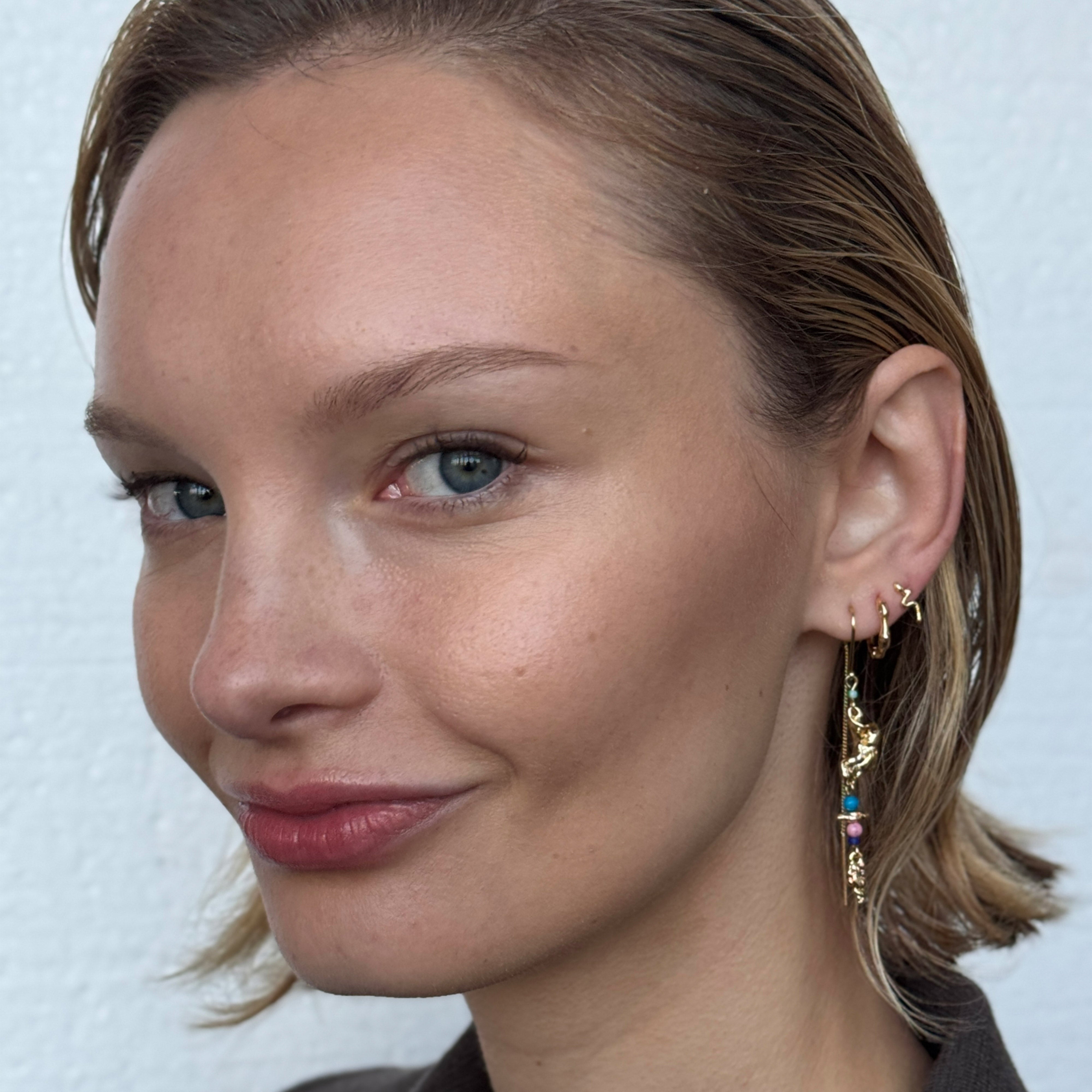Woman smiling, showcasing the PRISKILLA single earring, gold-plated, with a snake-inspired twist, highlighting Pilgrim's blend of elegance and mystery.