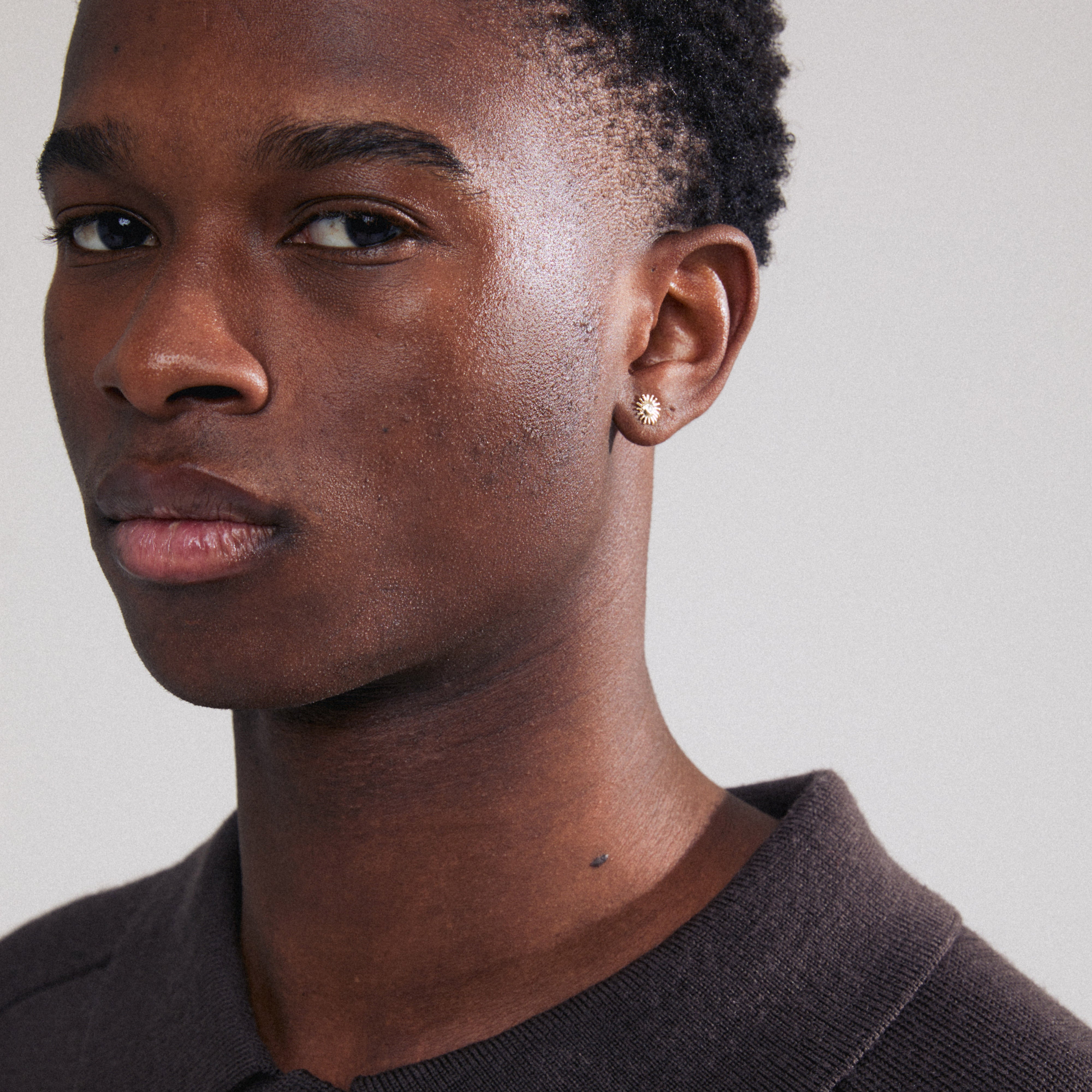 LAMIA single gold-plated earring, sun-shaped with a Preciosa crystal center, visible on a man's ear, showcasing trendy, Scandinavian-inspired style.
