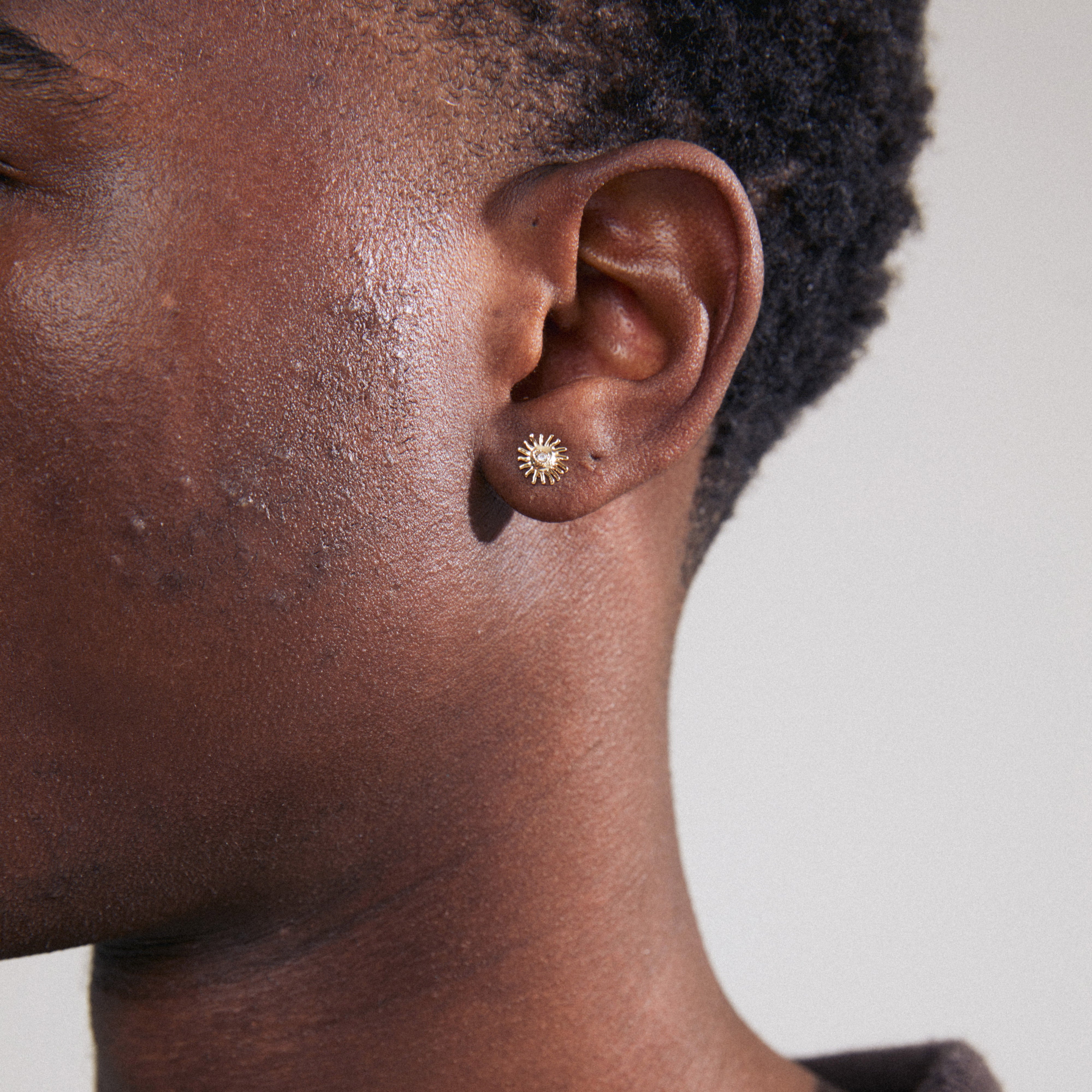 LAMIA single earring gold-plated, resembling a radiant sun with a Preciosa crystal center, adorning a close-up of a person's ear.