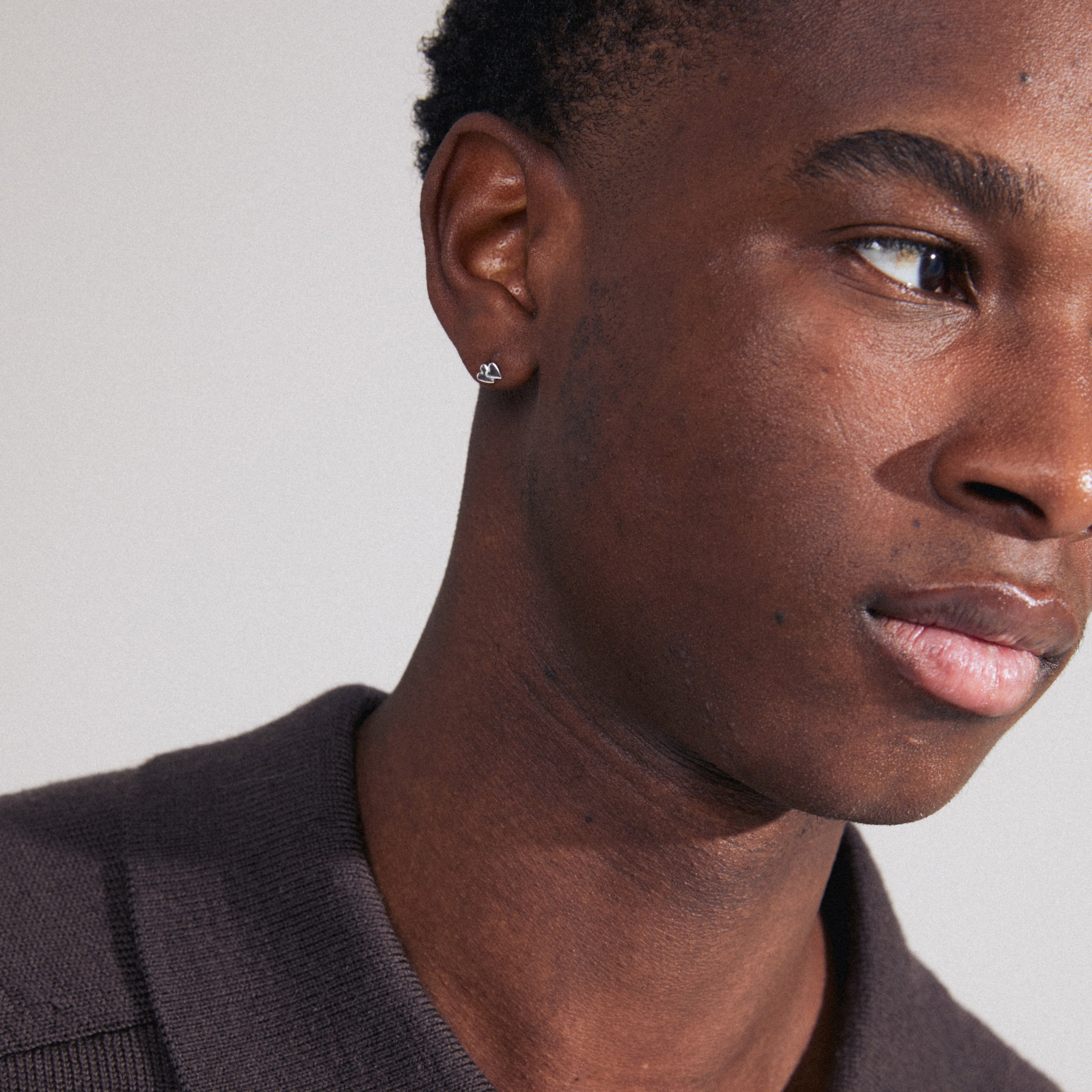 PRISKA single earring silver-plated, shaped like two tiny hearts, worn by a man showcasing detailed facial features. Made from 98% recycled material.