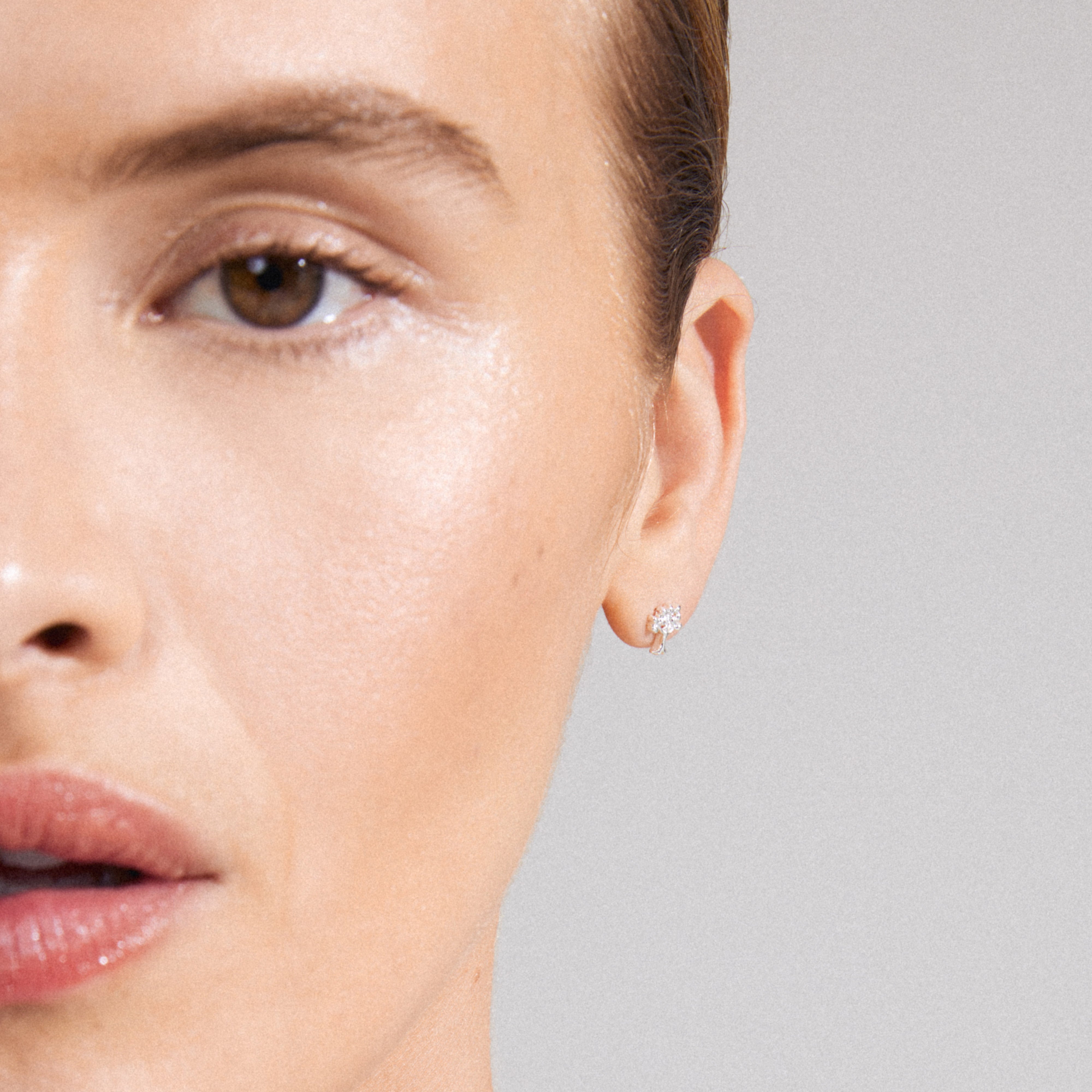 Close-up of a woman's ear wearing the PHYLLIS single earring, silver-plated with a tree of life design, emphasizing growth and connection.