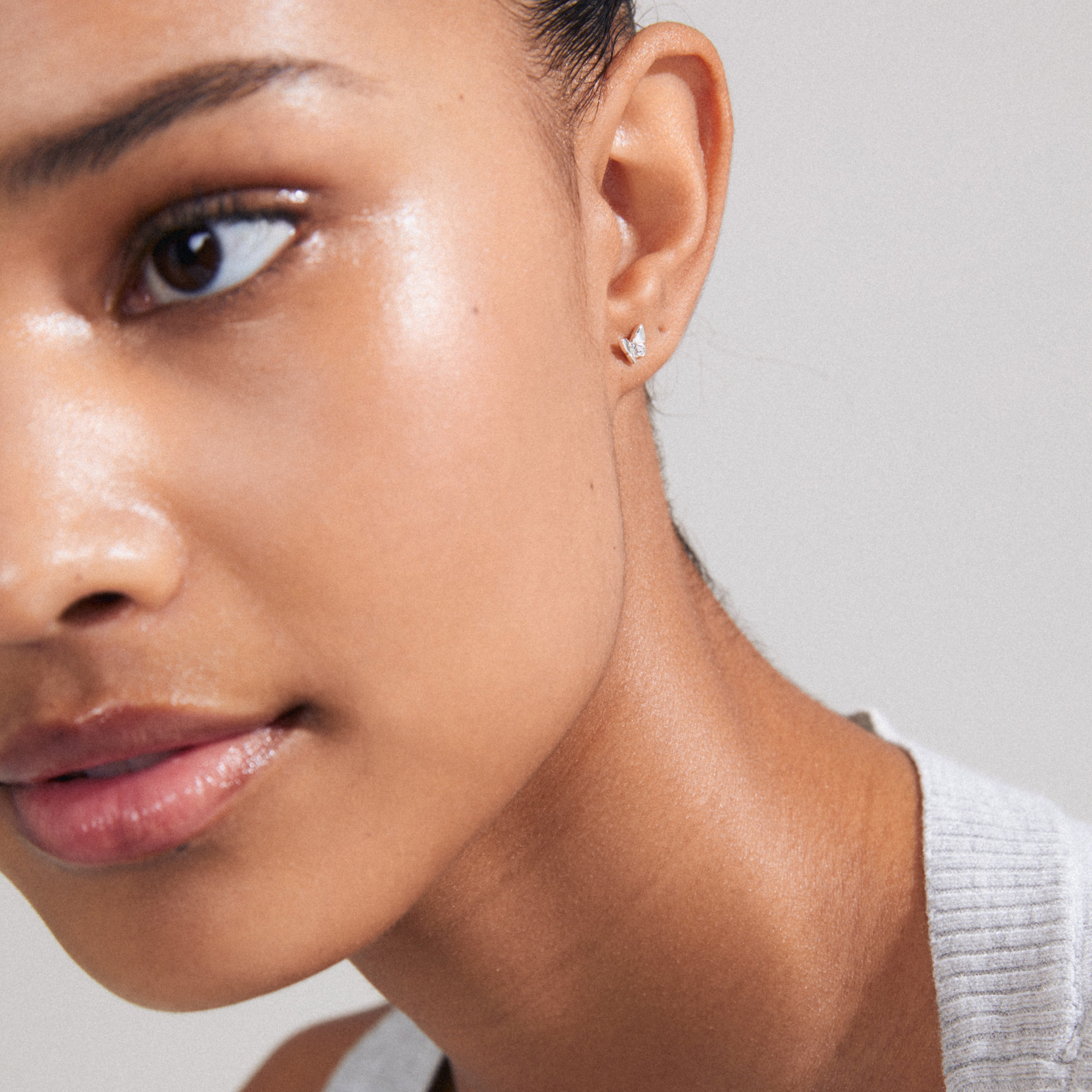 Close-up of a woman's face wearing the OLYMPIA silver-plated single earring, featuring a delicate butterfly design with Preciosa crystals.