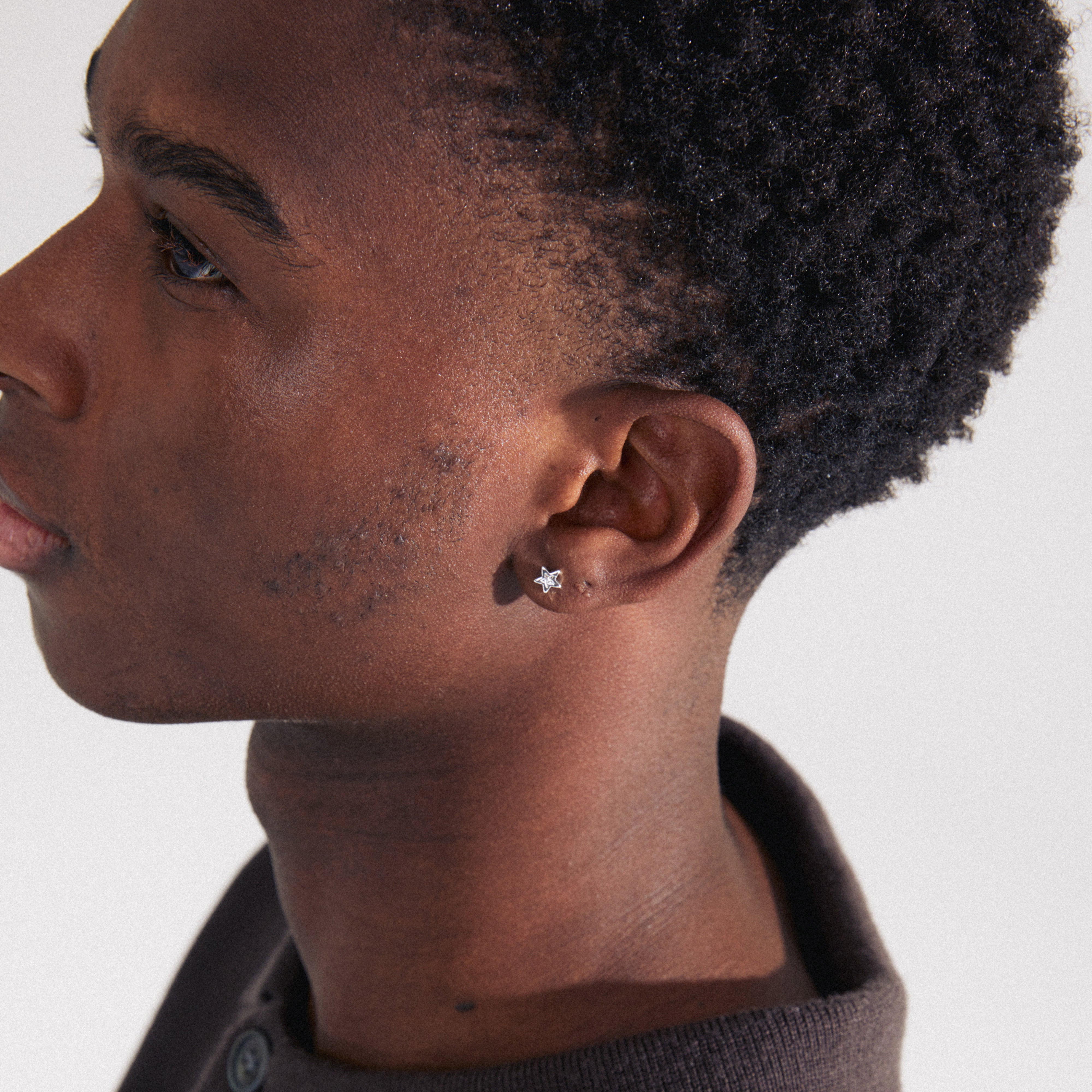 Man wearing a brown sweater showcases the NYX single earring, silver-plated with a Preciosa crystal, highlighting its sparkle and trendy design potential.