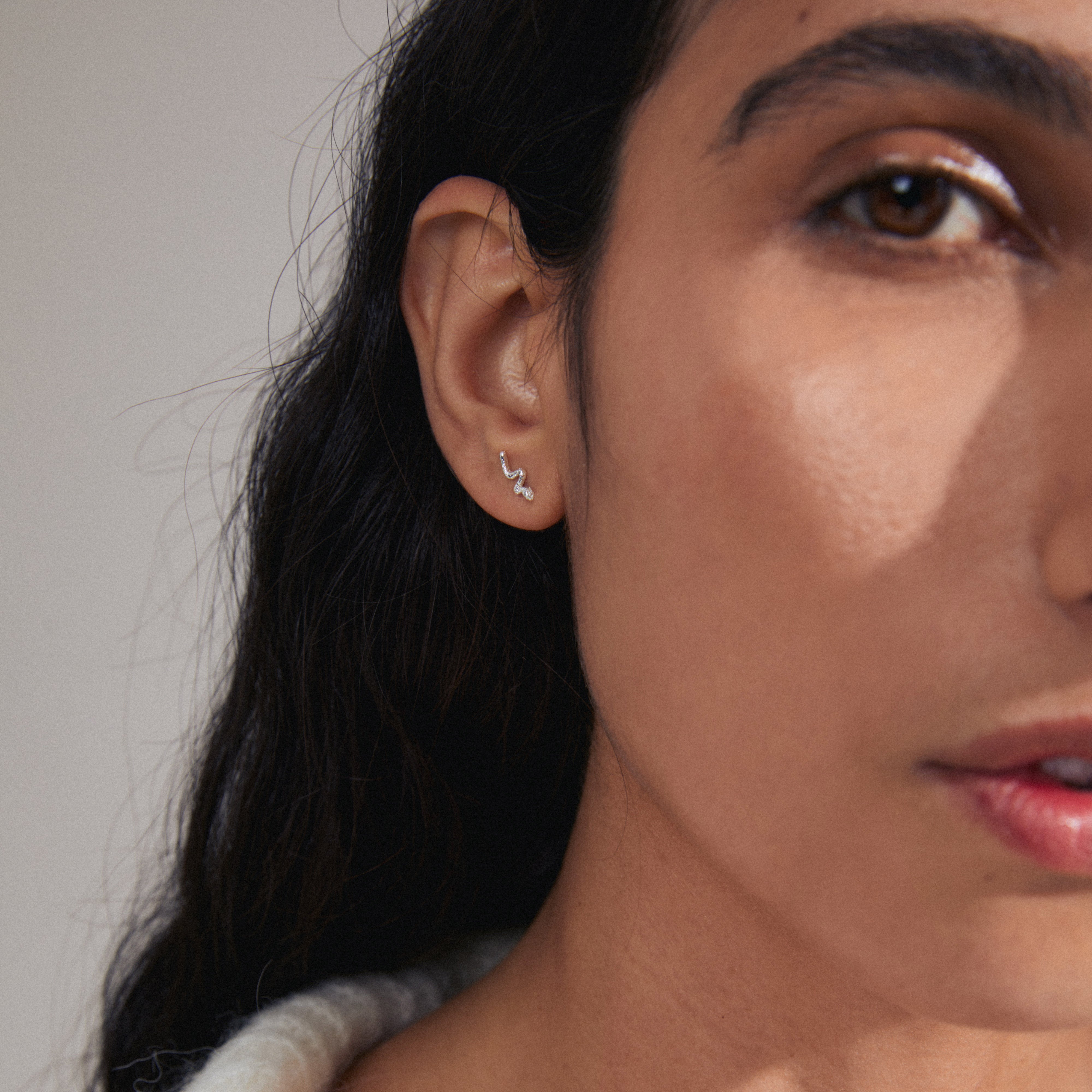 PRISKILLA single earring silver-plated, shaped like a snake, symbolizing renewal, crafted from 98% recycled materials, elegantly adorns a woman's ear.
