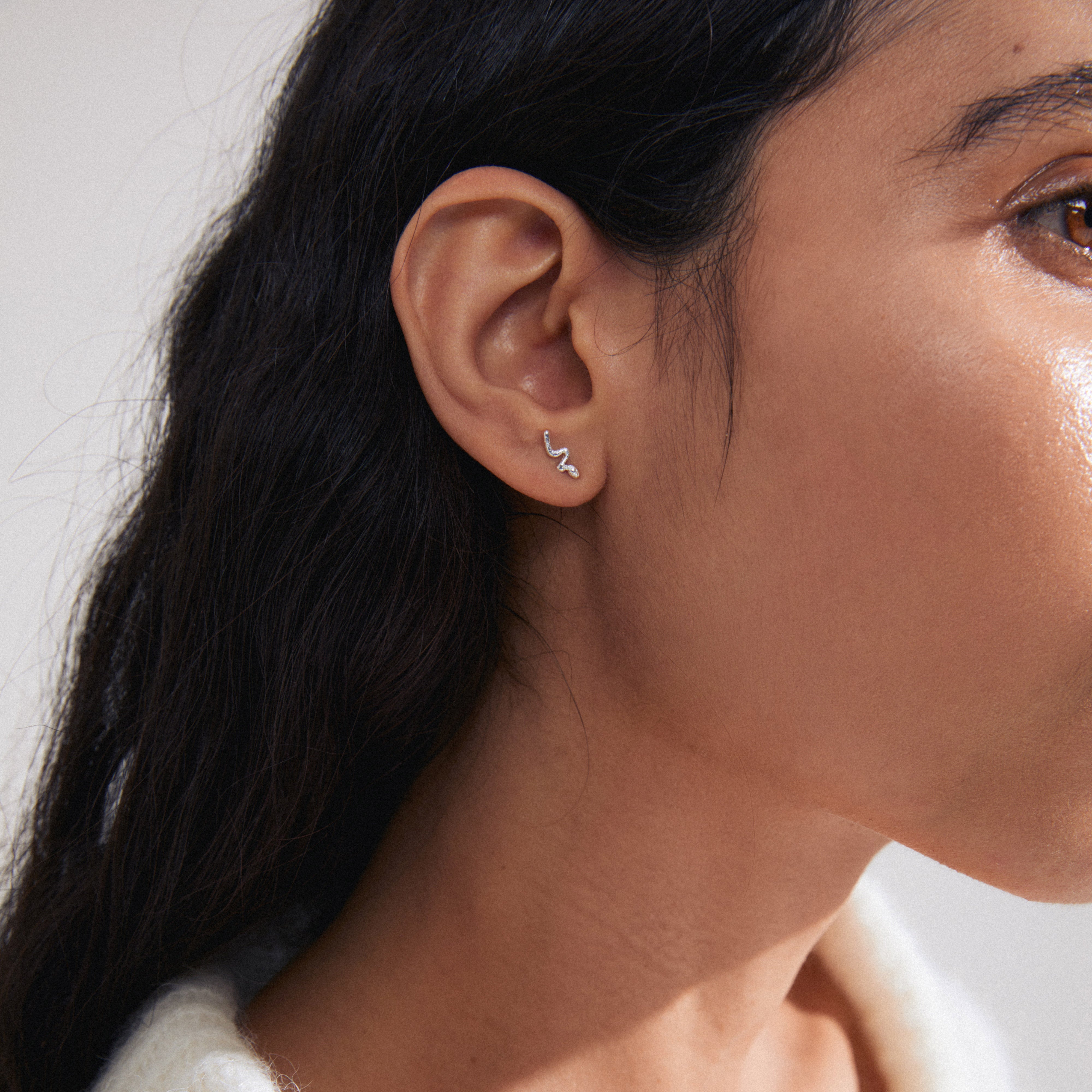 Close-up of a woman's ear wearing the PRISKILLA single earring, silver-plated with a snake-inspired twist, symbolizing renewal and transformation.
