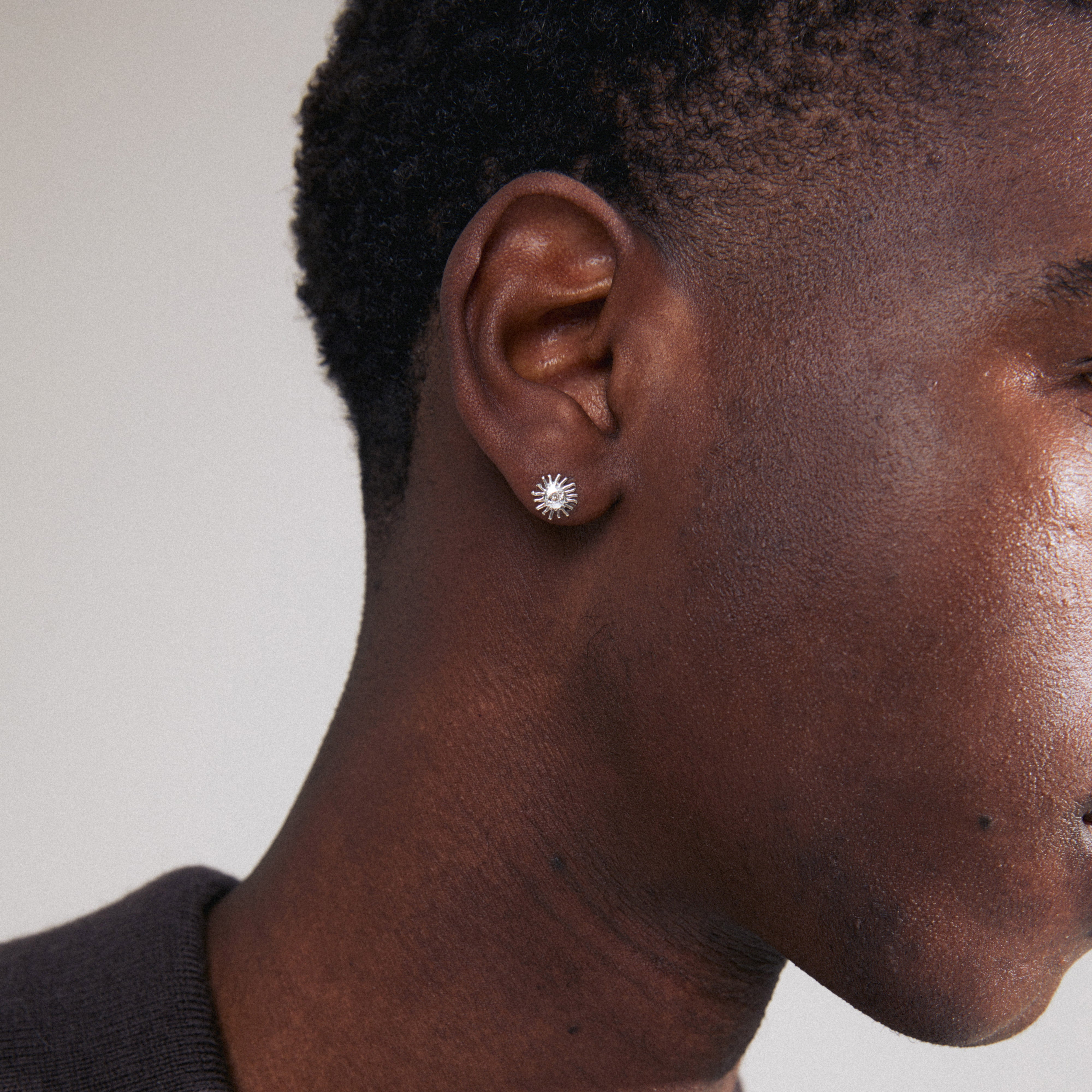 LAMIA single earring: silver-plated stud shaped like a radiant sun with a Preciosa crystal center, shown in a close-up on a man's ear.