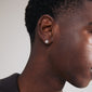 LAMIA single earring: silver-plated stud shaped like a radiant sun with a Preciosa crystal center, shown in a close-up on a man's ear.