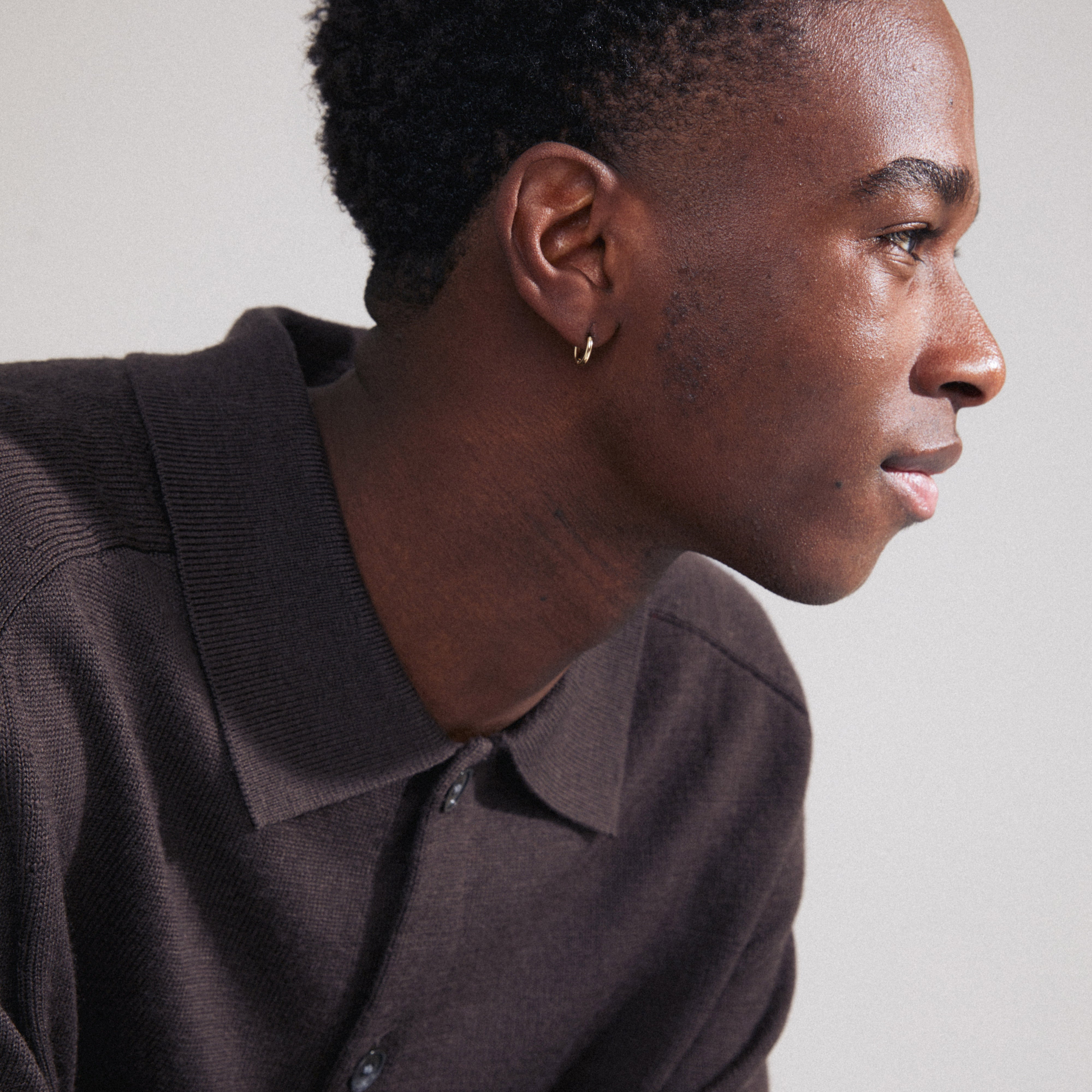 LAVRA single earring gold-plated, worn by a man with short curly hair. Features a small gold-plated huggie hoop with a shiny finish and click clasp.