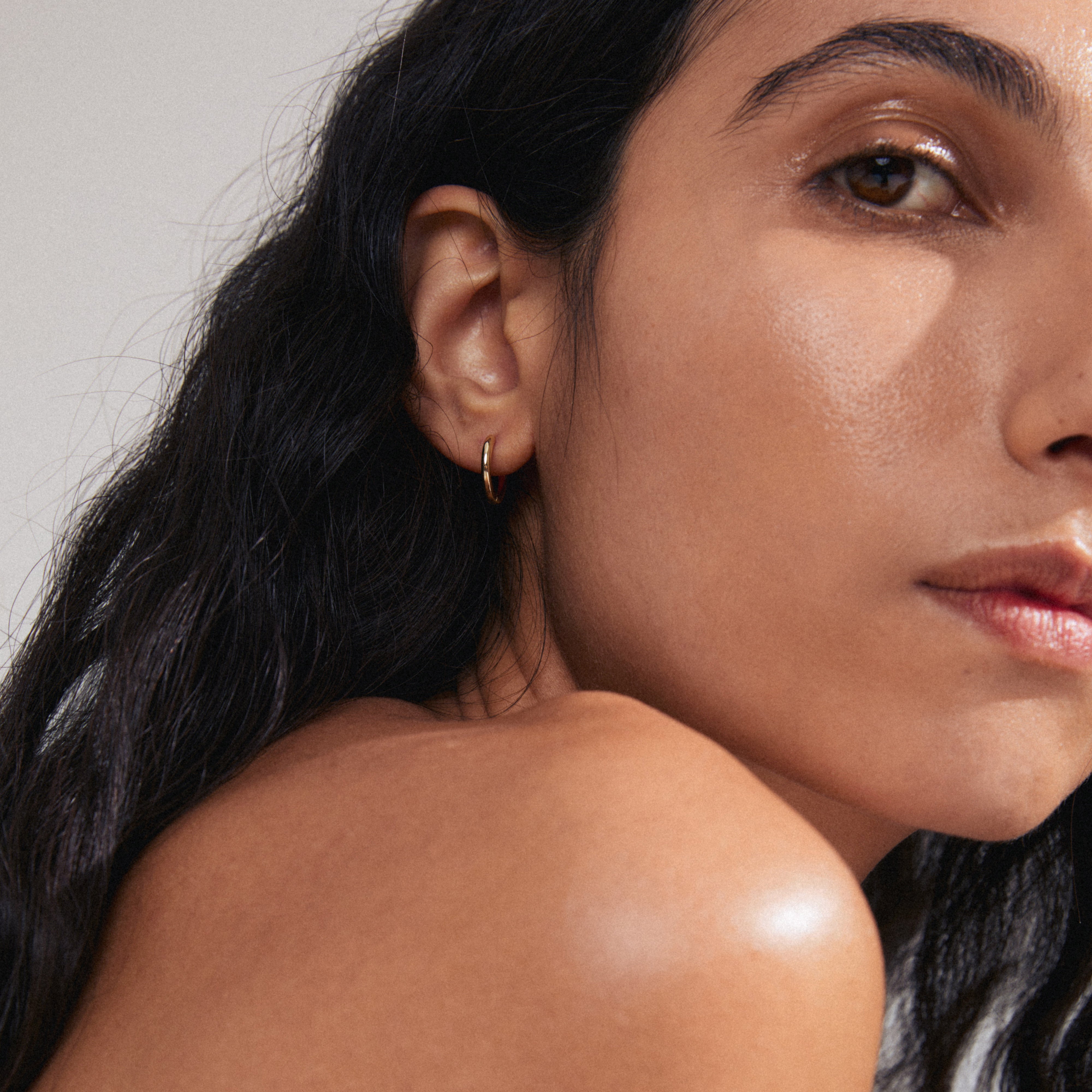 LAVRA single gold-plated earring showcased on a model's ear, featuring a shiny finish and classic hoop design, perfect for modern, asymmetrical styling.