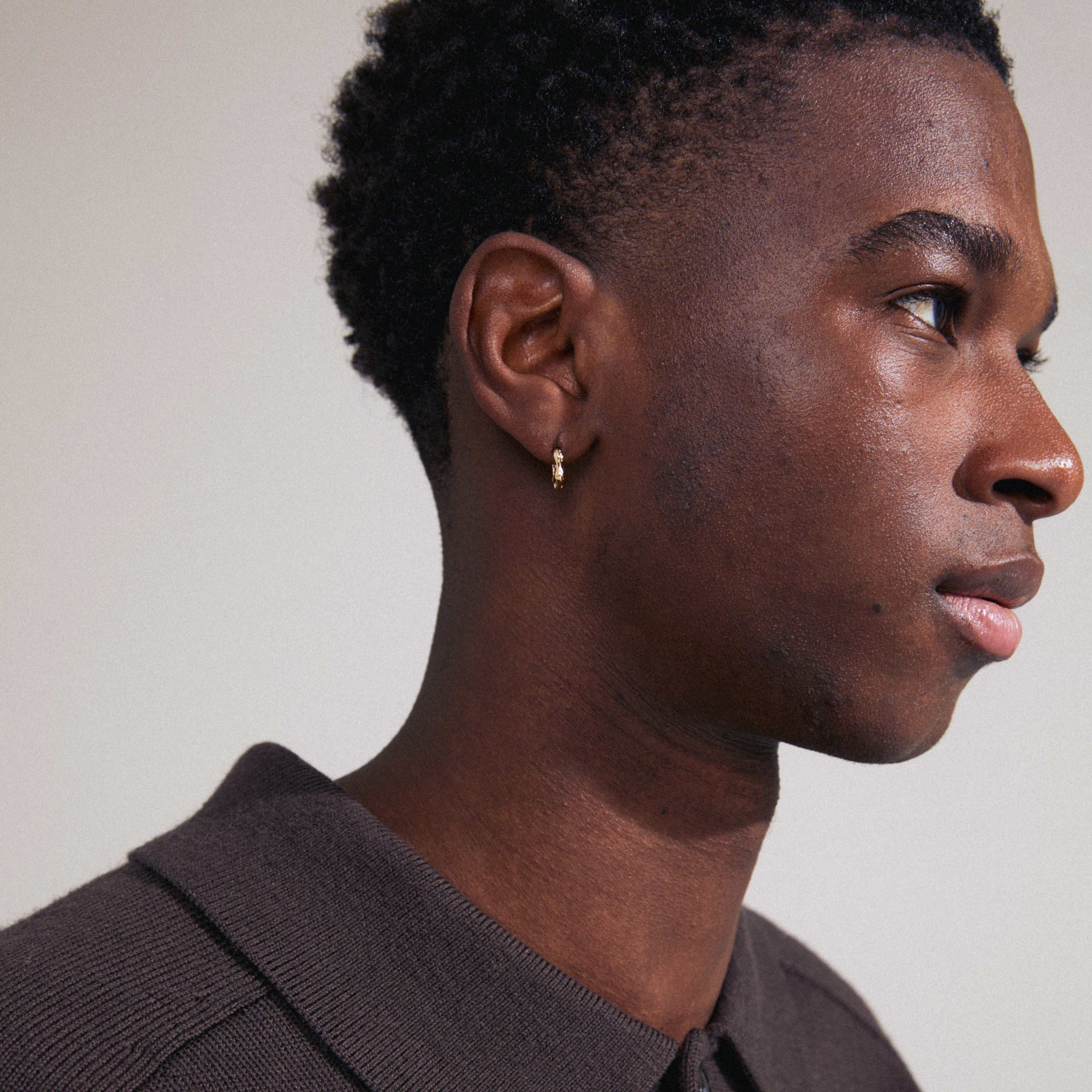 KYRA single earring gold-plated, showcased on a man, features a small, shiny, organic-shaped hoop with a click clasp, highlighting its handcrafted and timeless design.