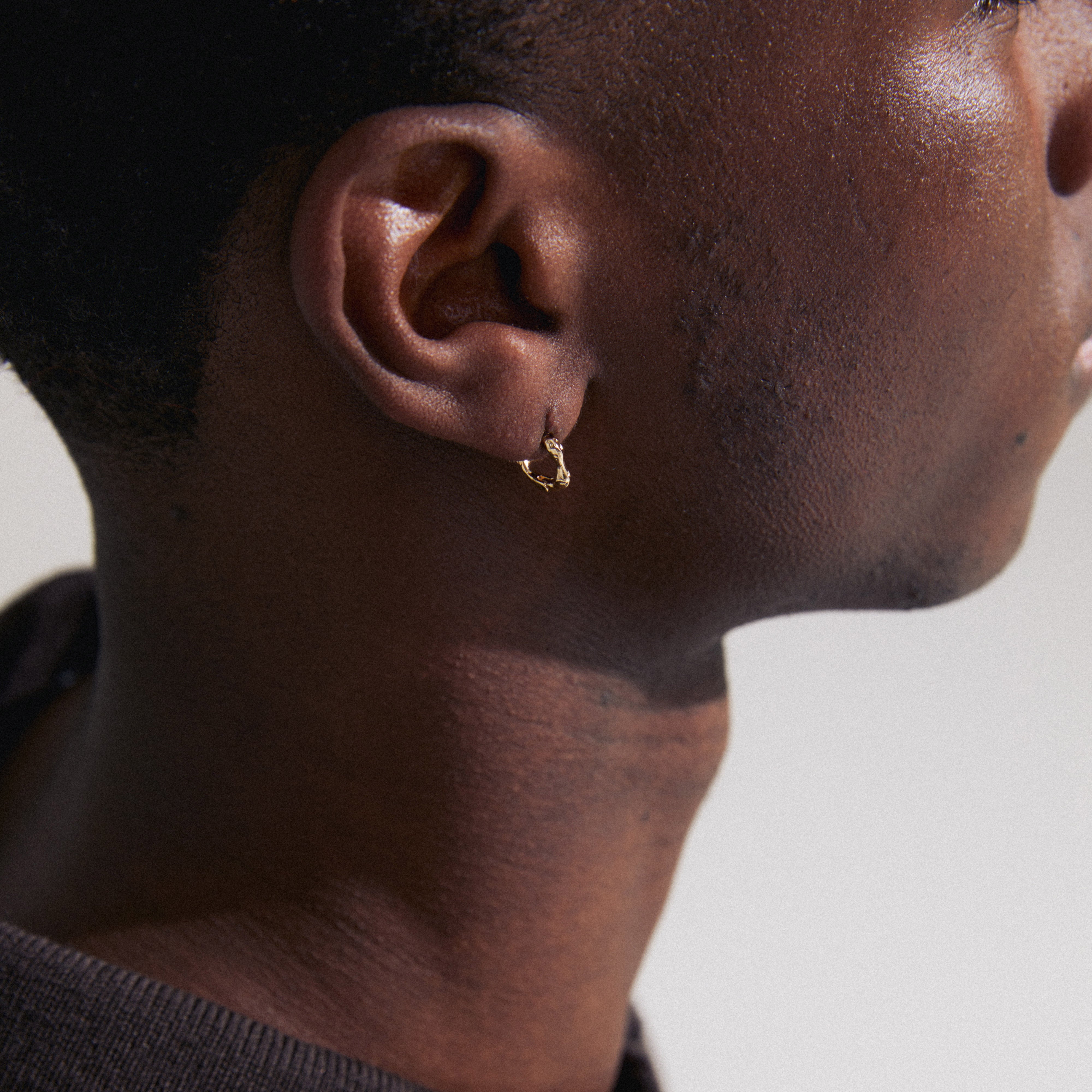KYRA single earring gold-plated on a person's ear, showcasing its organic shape and shiny, handcrafted finish with a click clasp.