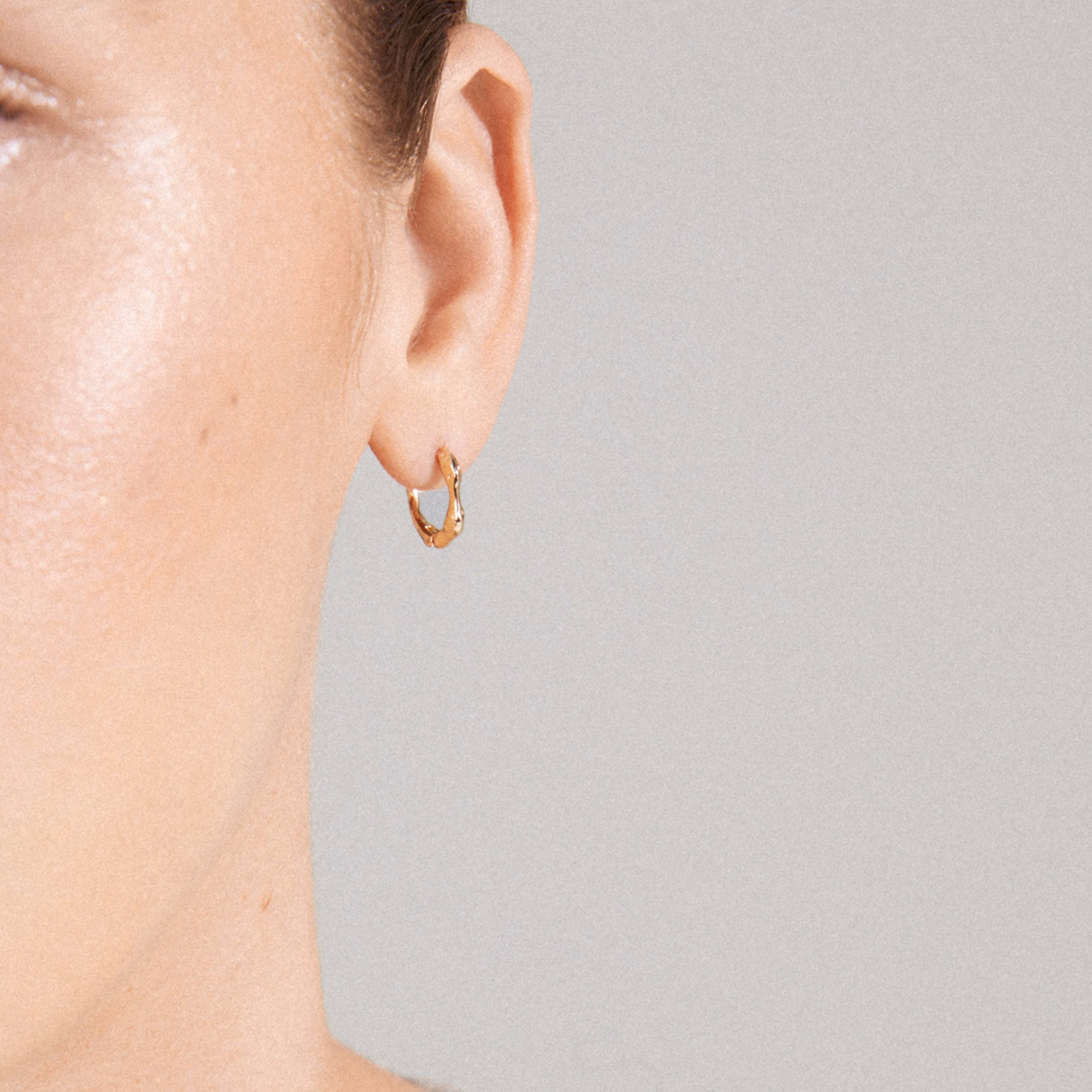 KYRA single earring gold-plated, featuring a small, textured hoop with a shiny finish and click clasp, elegantly showcased on a person's ear.
