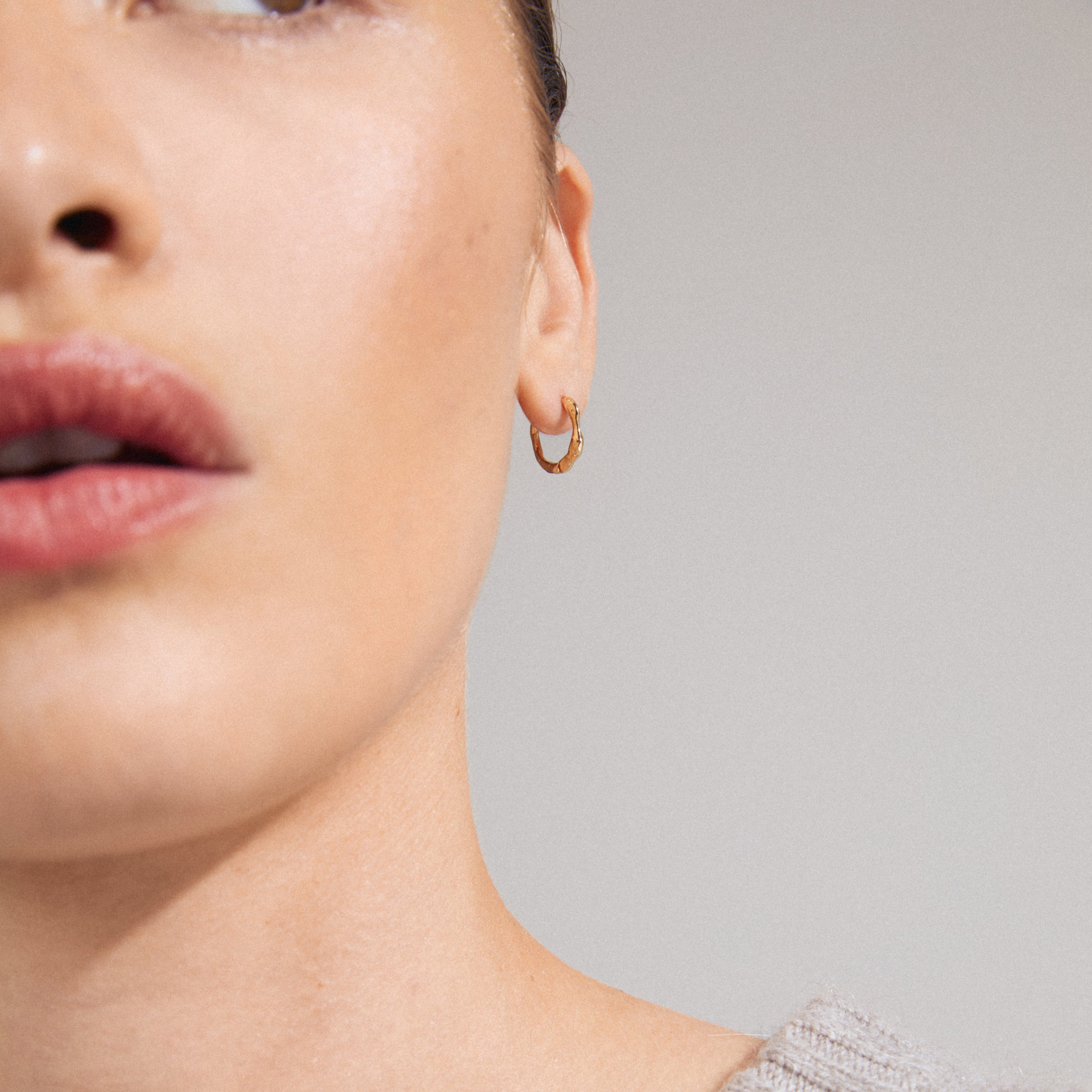 KYRA single earring gold-plated displayed on a woman, showcasing its shiny, organic shape and handcrafted vibe. Made from 99% recycled material with a click clasp.