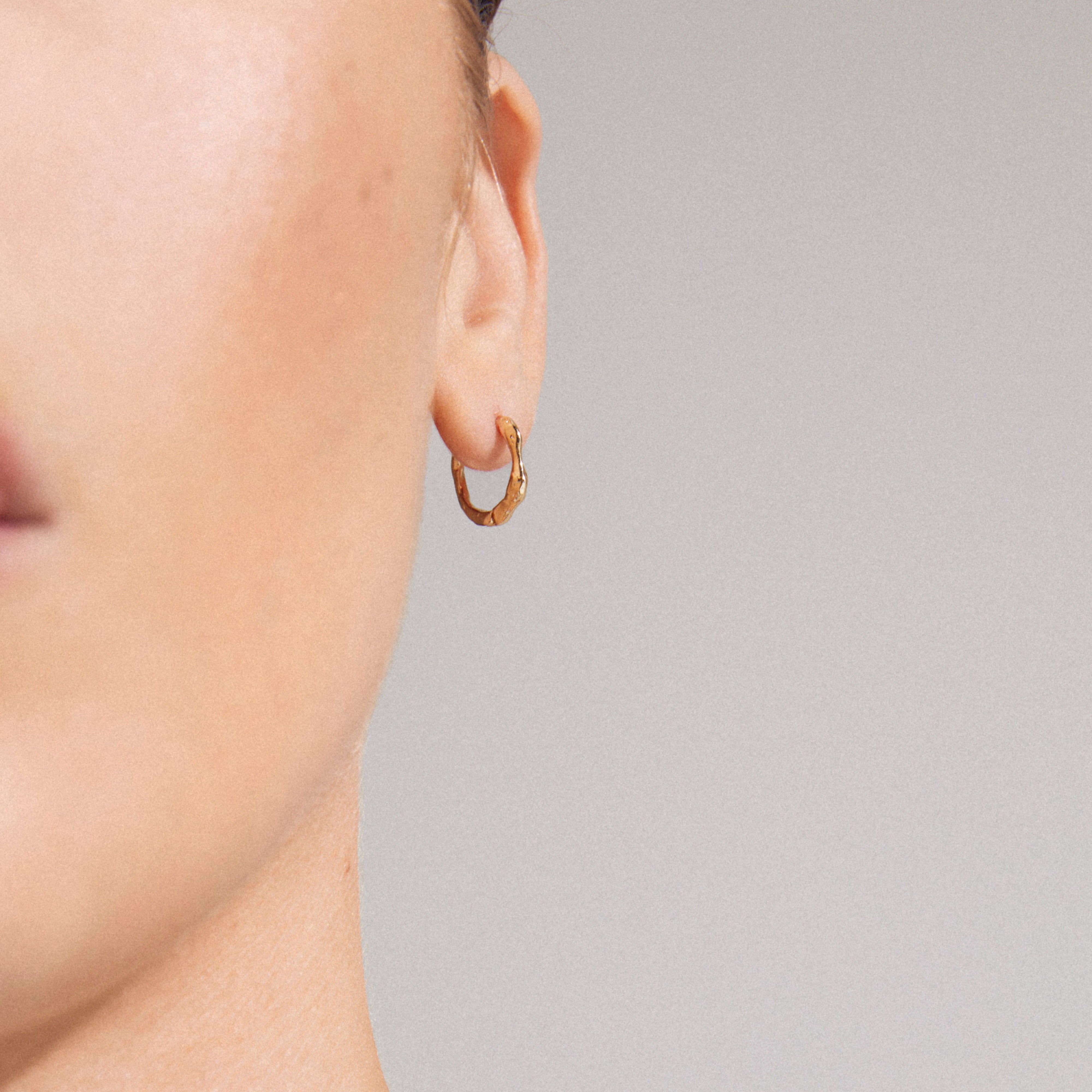 KYRA single earring gold-plated, textured hoop with an organic shape, showcased on an ear. Handcrafted, shiny finish, easy click clasp, made from recycled materials.